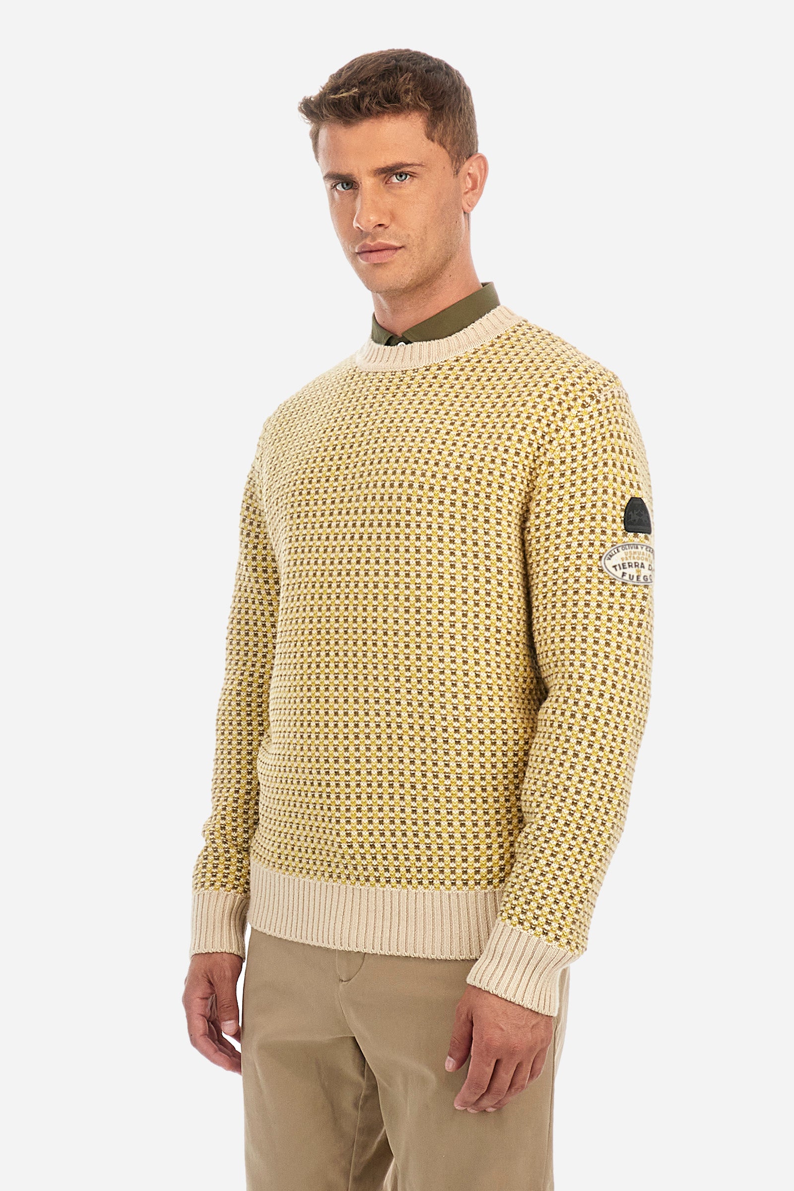 Men's crewneck pullover with long sleeves, made from a wool-blend yarn. The jacquard pattern differs on the front and sleeves, featuring a micro-check effect, while the back showcases a larger pattern with horizontal blocks. The collar, hem, and cuffs are in solid ribbed fabric. A patch inspired by Tierra del Fuego and a rubberized logo patch are applied on the sleeve. The fit is comfortable. - Jacquard Multicolour