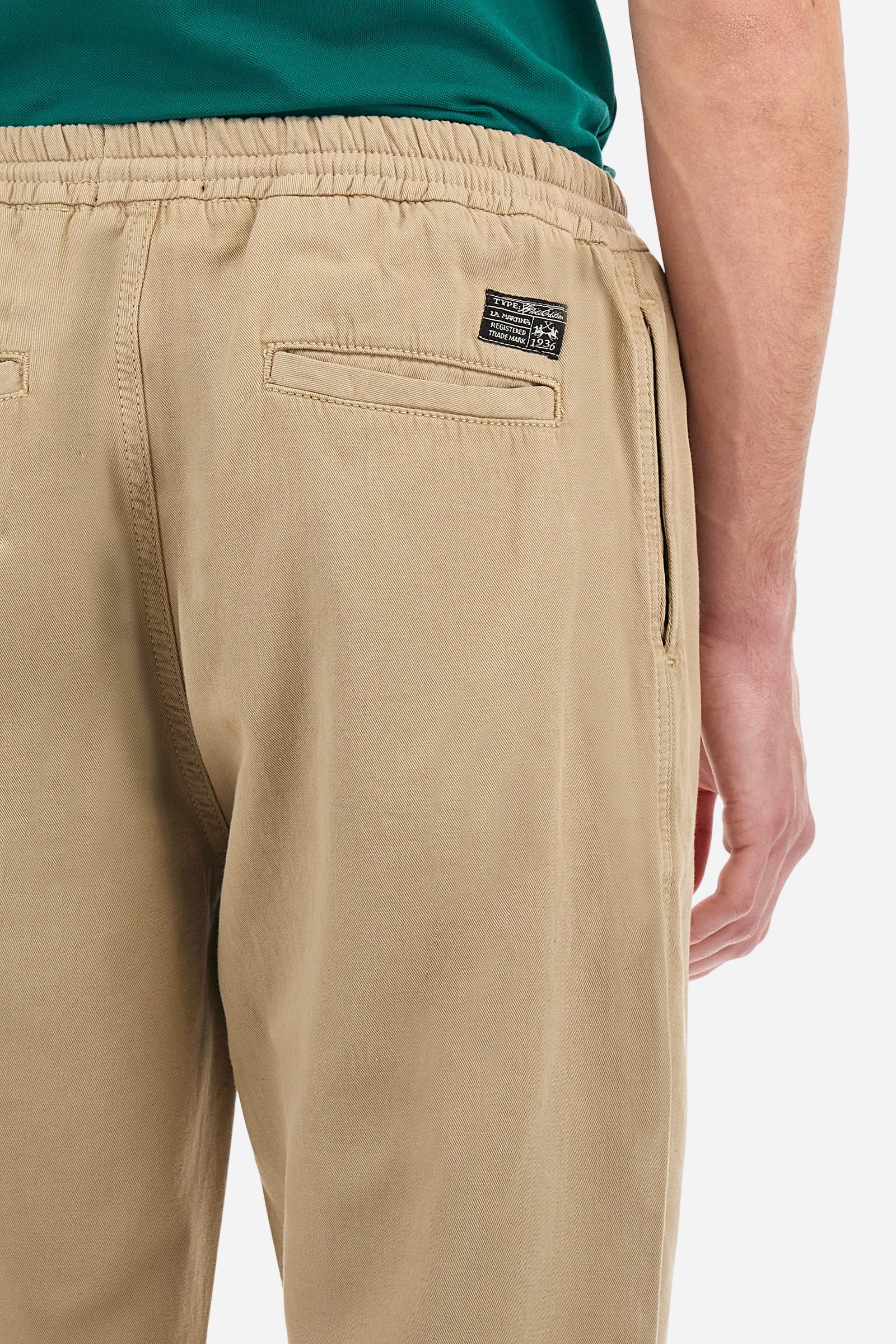 Men's plain straight-cut trousers, made of linen and cotton canvas. Featuring a waist belt at the back and on the sides with elasticated external drawstring for adjustment. The front opening also has a faux horn button on the belt and a zip. Double welt pocket inserted into the sides. There are two additional welt pockets on the back. The logo is featured on the woven label sewn above the right back pocket. Regular fit. The model is wearing a size L. - Twill