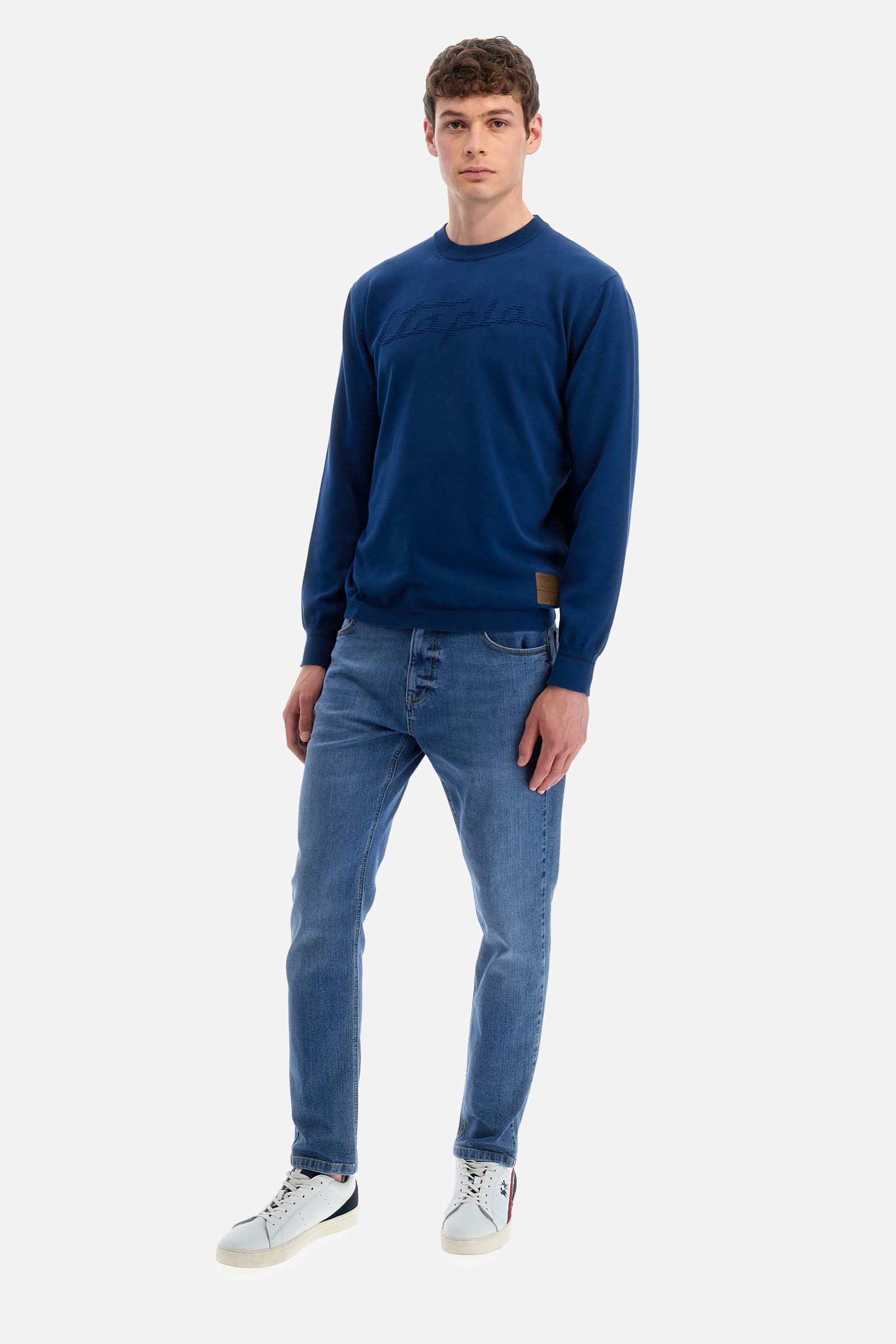 Men's long-sleeved crew-neck jumper in a single colour in collaboration with Pagani. Made from 100% cotton. Some parts of the garment have a woven basket stitch texture. Ribbed cuffs, neck and waist. The front features the line's characteristic lettering. The logo and "La Martina" and "Pagani" lettering are present on the patch representing the collaboration applied on both the front and back. The fit is regular. The model wears a size L. - Ensign Blue