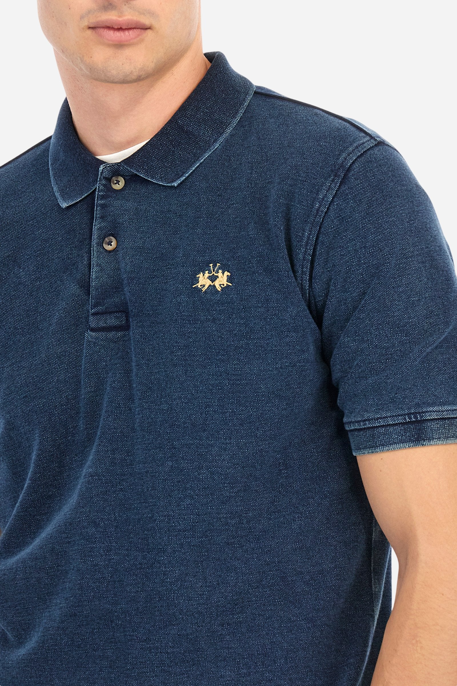 Men's short-sleeved polo shirt made of 100% cotton indigo pique. Fastens with two buttons. The collar and cuffs are folded and are made of ribbed fabric. Garment treated with enzyme washing, which gives the faded and lived-in look typical of denim. The contrasting embroidered logo is present on the left side of the chest. Regular fit. The model is wearing a size L. - Dark Indigo Denim