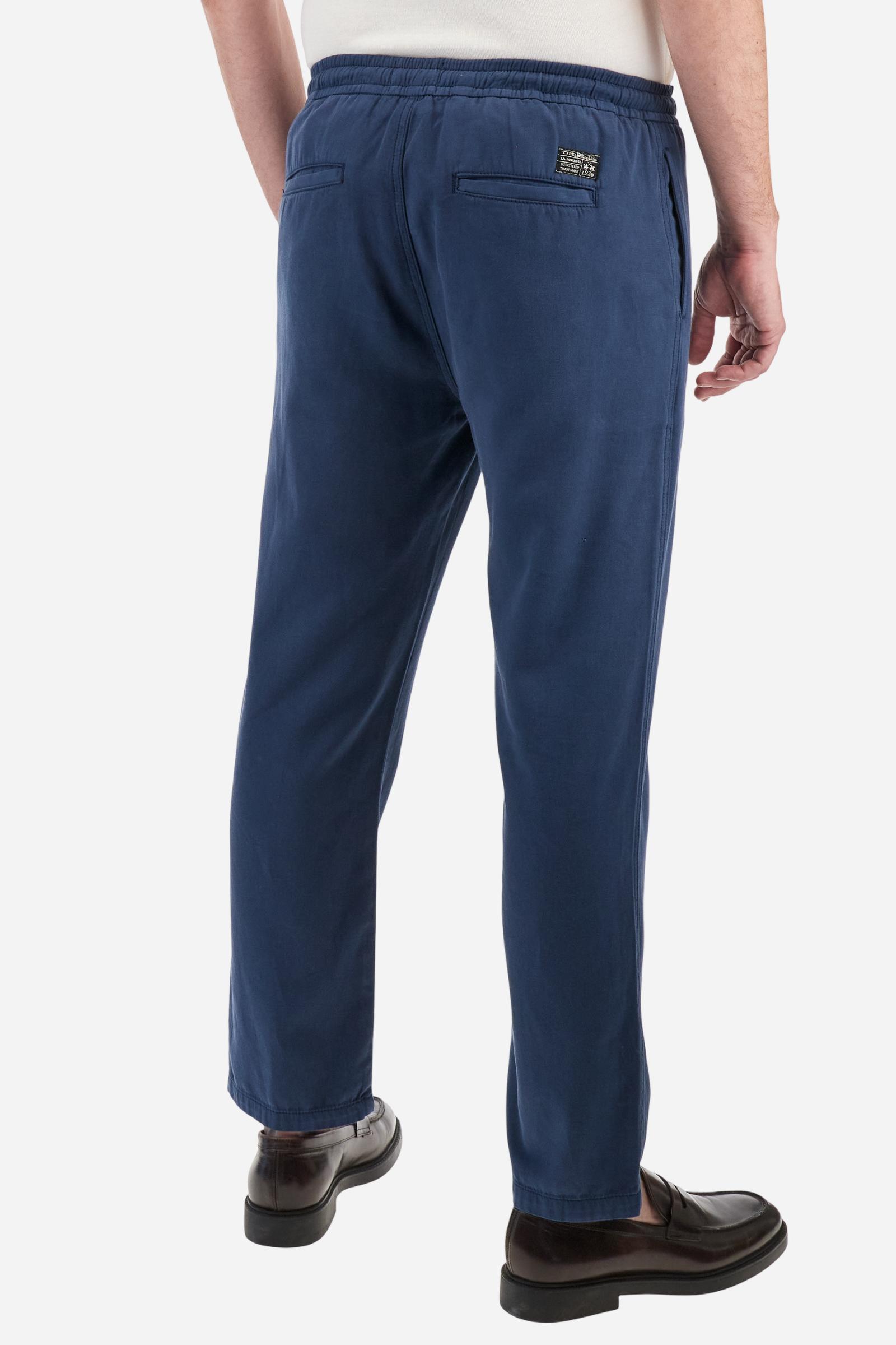 Men's plain straight-cut trousers, made of linen and cotton canvas. Featuring a waist belt at the back and on the sides with elasticated external drawstring for adjustment. The front opening also has a faux horn button on the belt and a zip. Double welt pocket inserted into the sides. There are two additional welt pockets on the back. The logo is featured on the woven label sewn above the right back pocket. Regular fit. The model is wearing a size L. - Navy