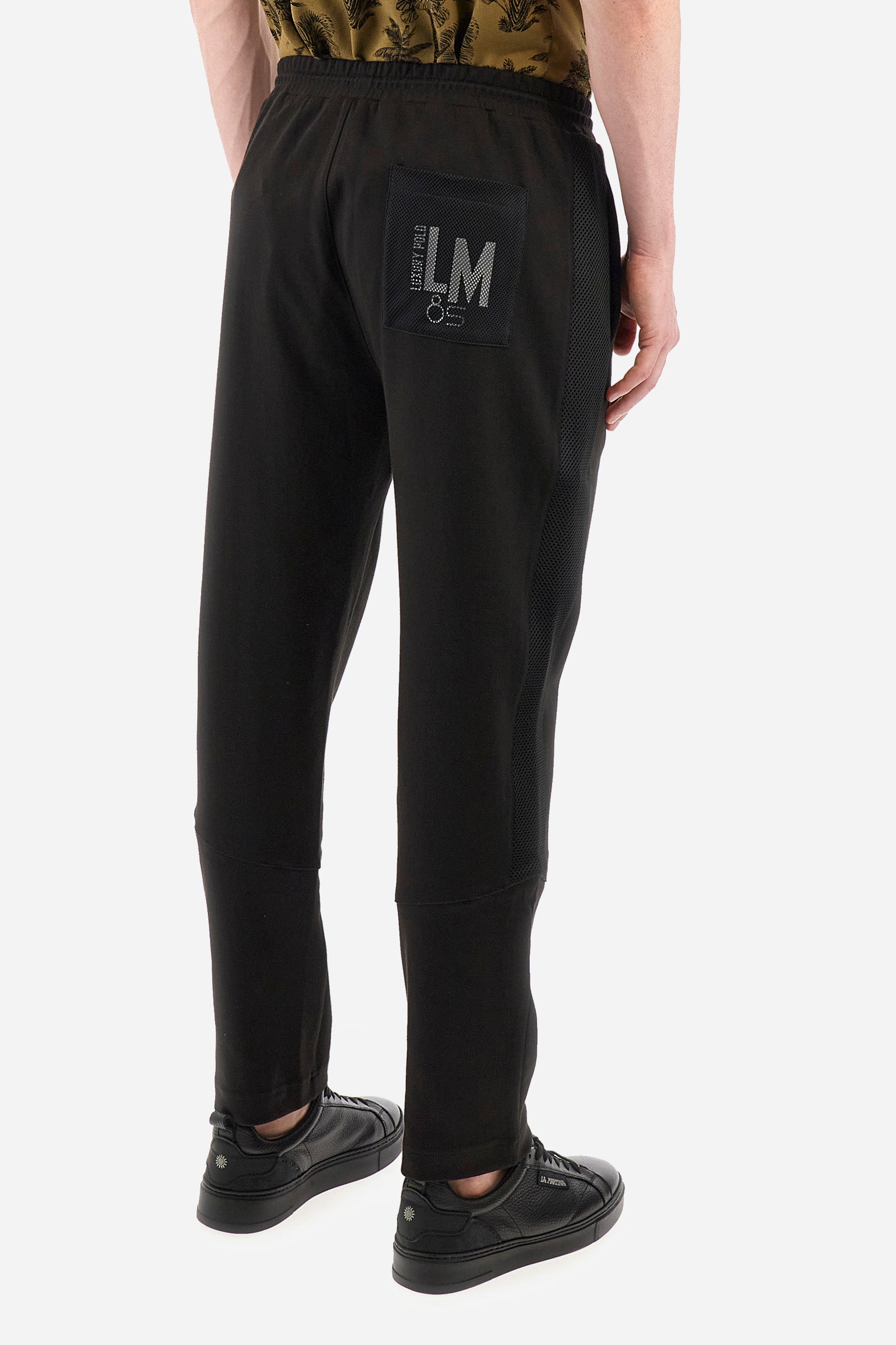 Men's single-colour jogging bottoms in mixed cotton. Drawstring at the waist and double welt pocket on the front. Featuring a side stripe with a honeycomb texture. On the back there is a single open pocket featuring the brand's initials. The fit is regular. The model wears a size L. - Black