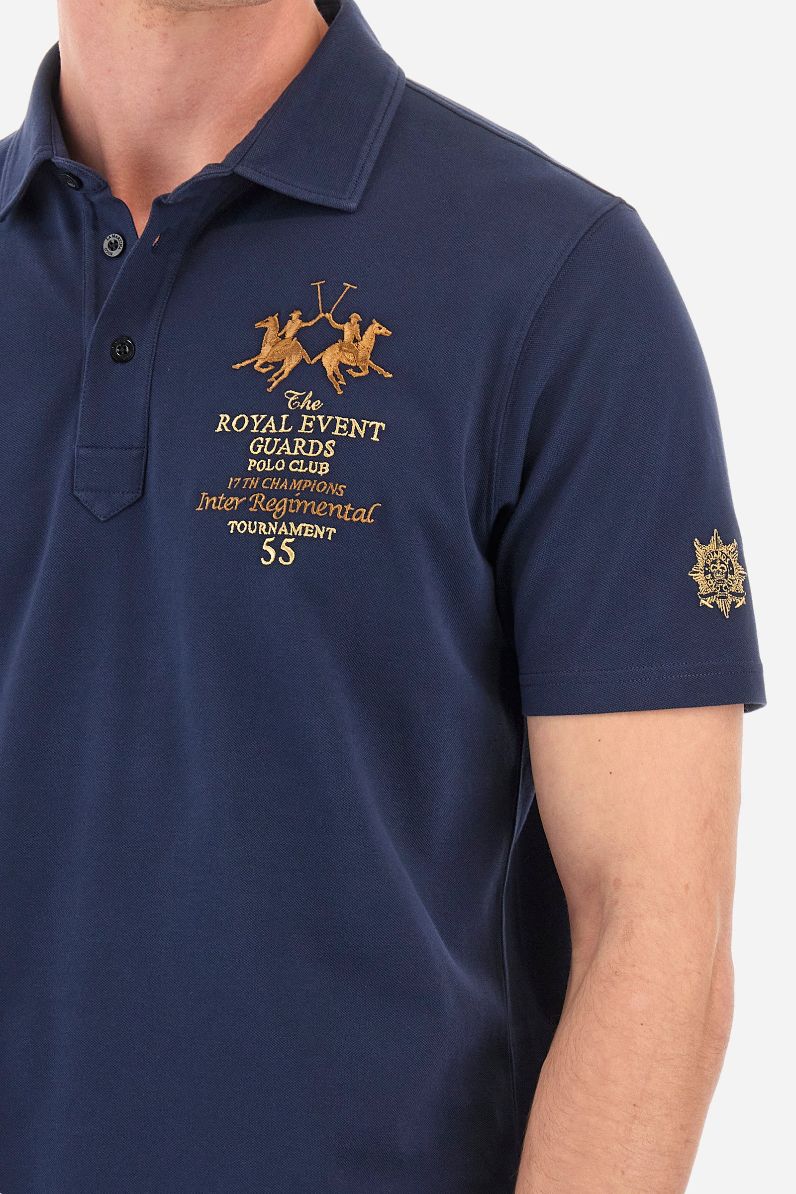 Men's short-sleeved single-colour polo shirt in elasticated cotton. Two-button fastening. Pointed collar. On the front we find copper-coloured lettering and a large logo. On one of the sleeves there is a symbol representing the Guards line. The fit is regular. The model wears a size L. - Navy