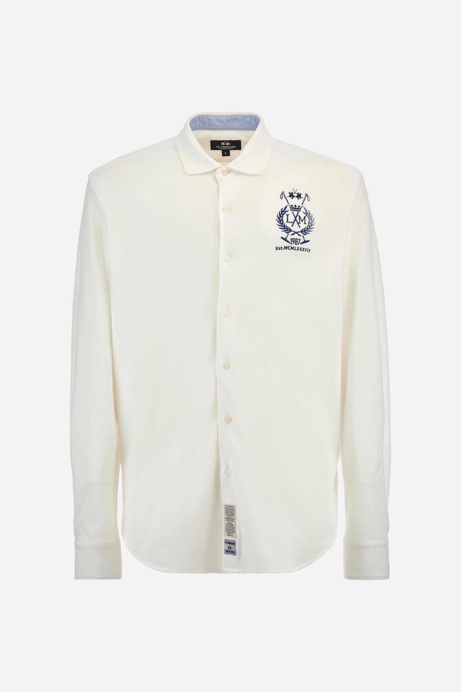 Men's plain long-sleeved shirt made from cotton piqué. It features an elegant spread collar and a seamless front opening, with no visible stitching. A graphic is embroidered on the chest, over the heart, in contrasting thread. Regular fit. The model is wearing a size L. - Optic White