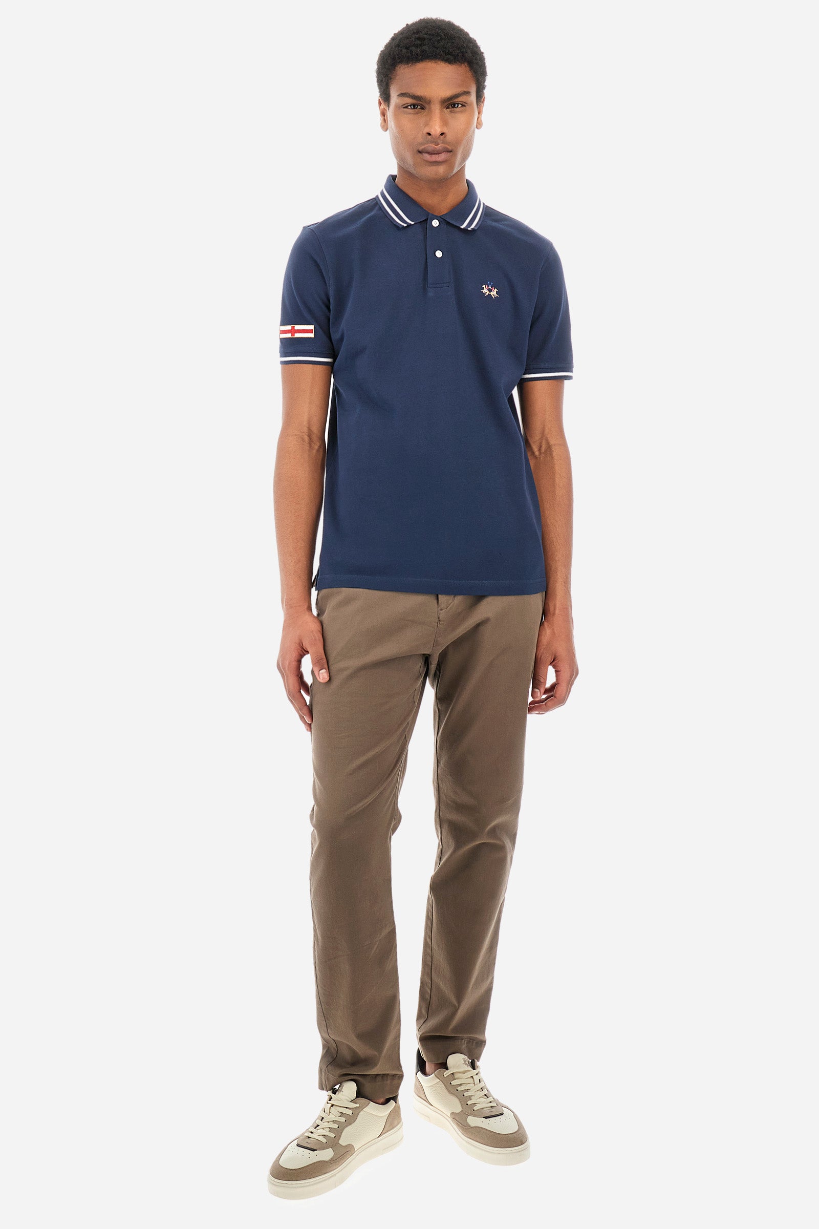 Men’s polo shirt in solid color with short sleeves in 100% cotton piquet. Two button closure. Edge and inner neck, along with the armhole all profiled with contrasting stripes. On one of the sleeves is applied a patch depicting the flag of the country to recall the capsule collection Ciudades. Small La Martina logo embroidered on the chest. The fit is regular. The model wears a size L. - Navy