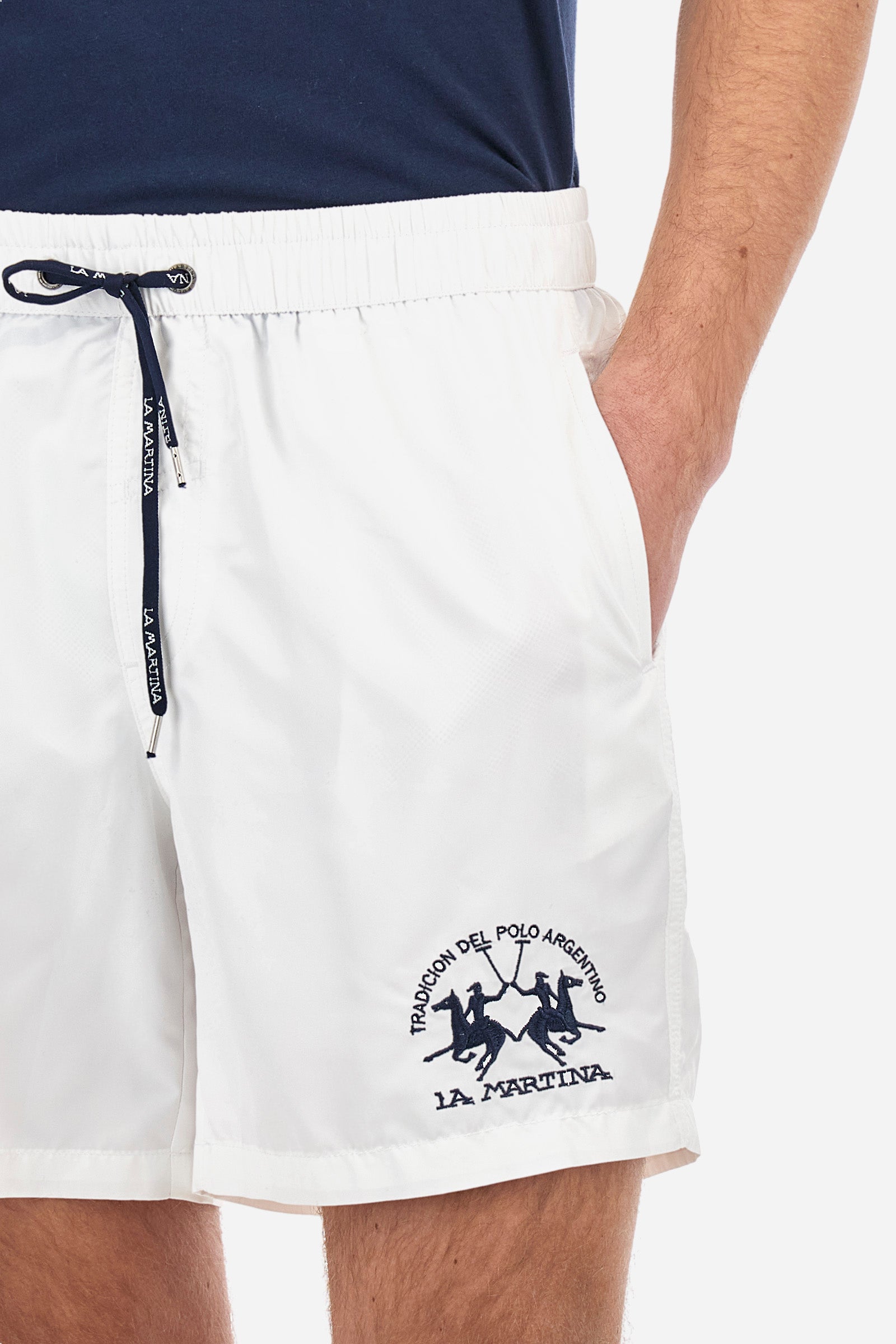 Plain men's swimming shorts made of nylon. Elastic waistband with a personalised drawstring for waist adjustment. On the inside of the shorts is an elasticated mesh brief. Double side pocket on the hips and patch pocket with flap on the back, on the right side only. The large logo is embroidered in a contrasting colour thread on the bottom of the left leg on the front. Regular fit. The model is wearing a size L. - Optic White