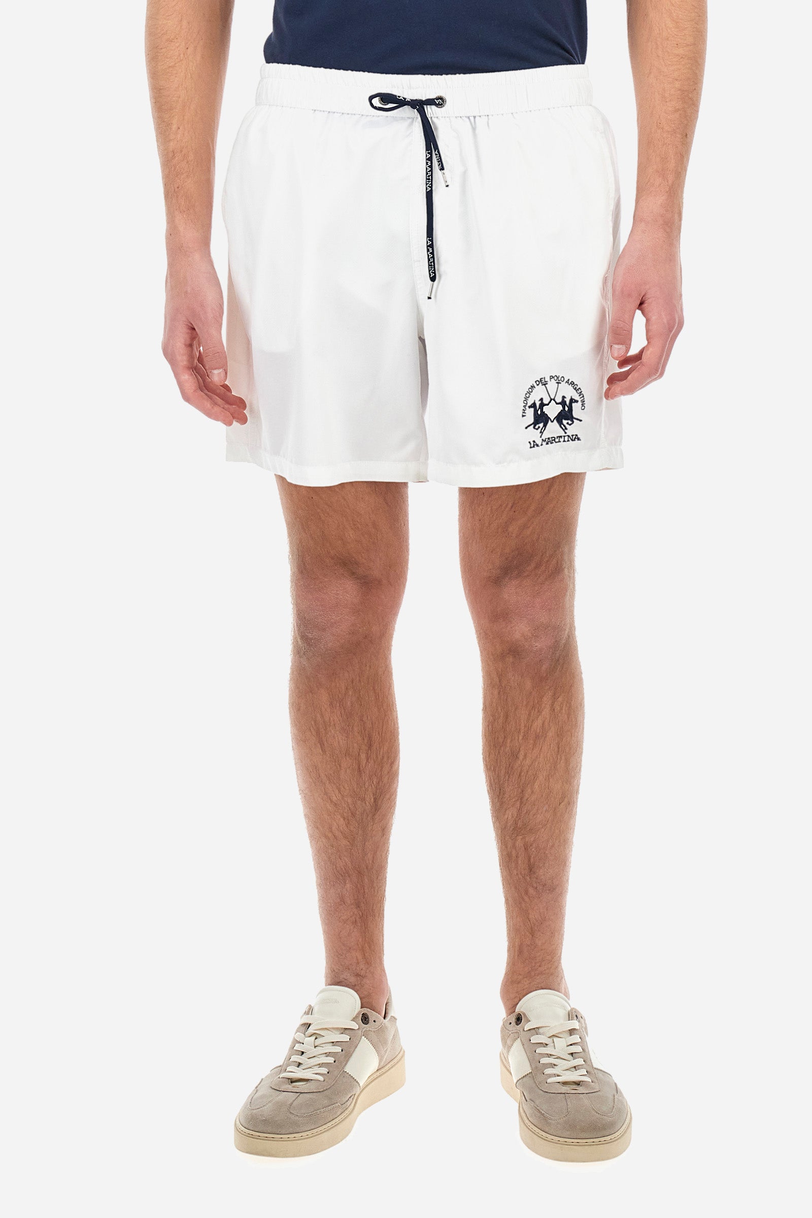 Plain men's swimming shorts made of nylon. Elastic waistband with a personalised drawstring for waist adjustment. On the inside of the shorts is an elasticated mesh brief. Double side pocket on the hips and patch pocket with flap on the back, on the right side only. The large logo is embroidered in a contrasting colour thread on the bottom of the left leg on the front. Regular fit. The model is wearing a size L. - Optic White