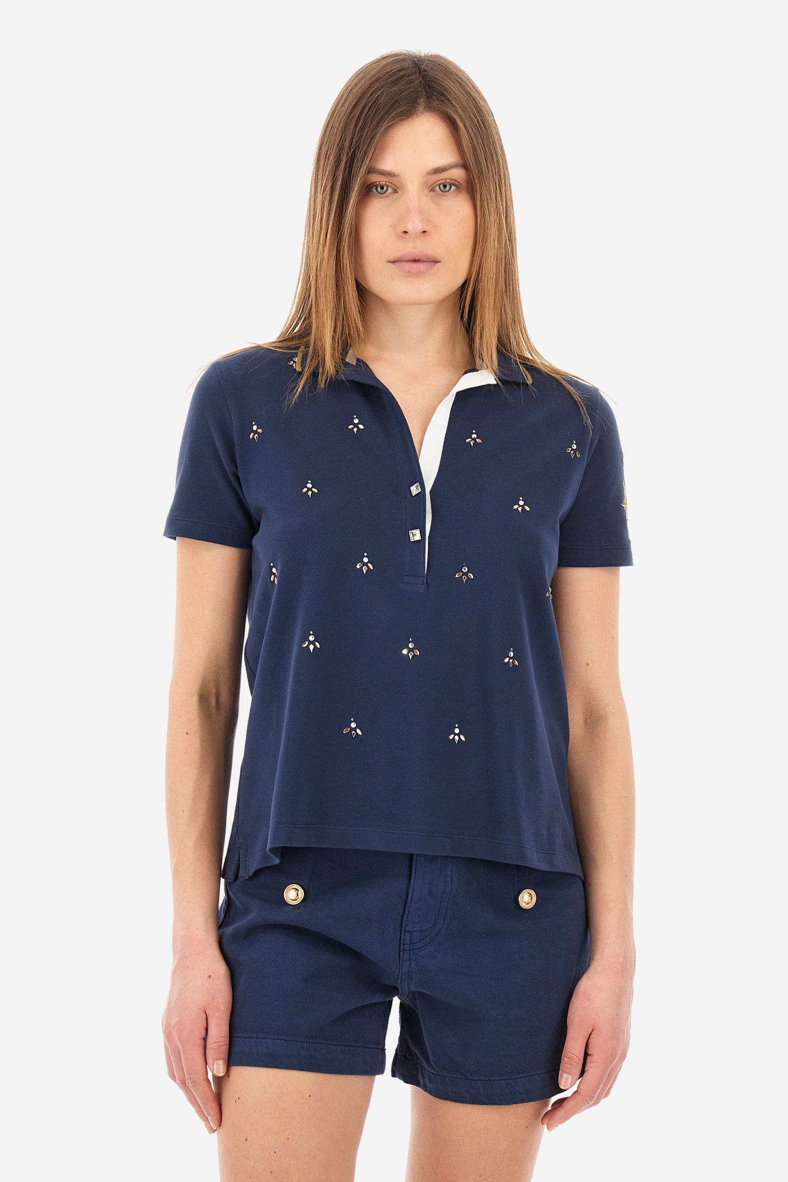 Women’s polo with short sleeves in solid color from the Guards line. Made of stretch cotton. V-neck and 2-button jewel closure. Ribbed collar. Side slits. Rhinestones of various shapes, sizes and colors were applied to the front. The logo and the characteristic symbol of the line are embroidered on a sleeve. The fit is regular. The model wears a size 2 . - Navy