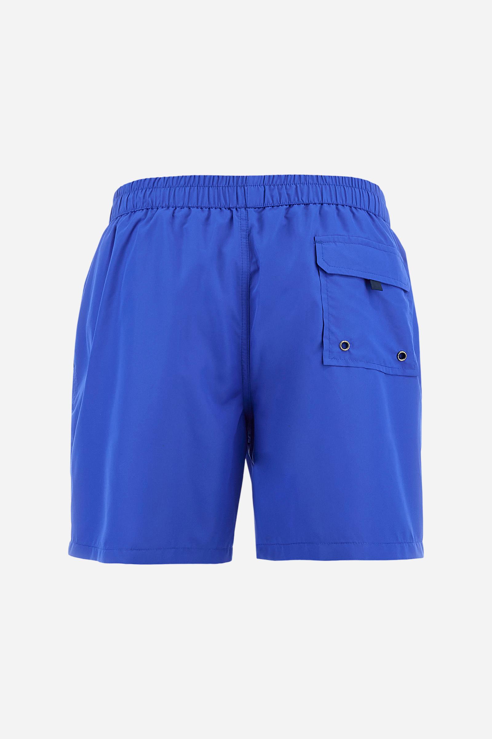 Plain men's swimming shorts made of nylon. Elastic waistband with a personalised drawstring for waist adjustment. On the inside of the shorts is an elasticated mesh brief. Double side pocket on the hips and patch pocket with flap on the back, on the right side only. The large logo is embroidered in a contrasting colour thread on the bottom of the left leg on the front. Regular fit. The model is wearing a size L. - Dazzling Blue