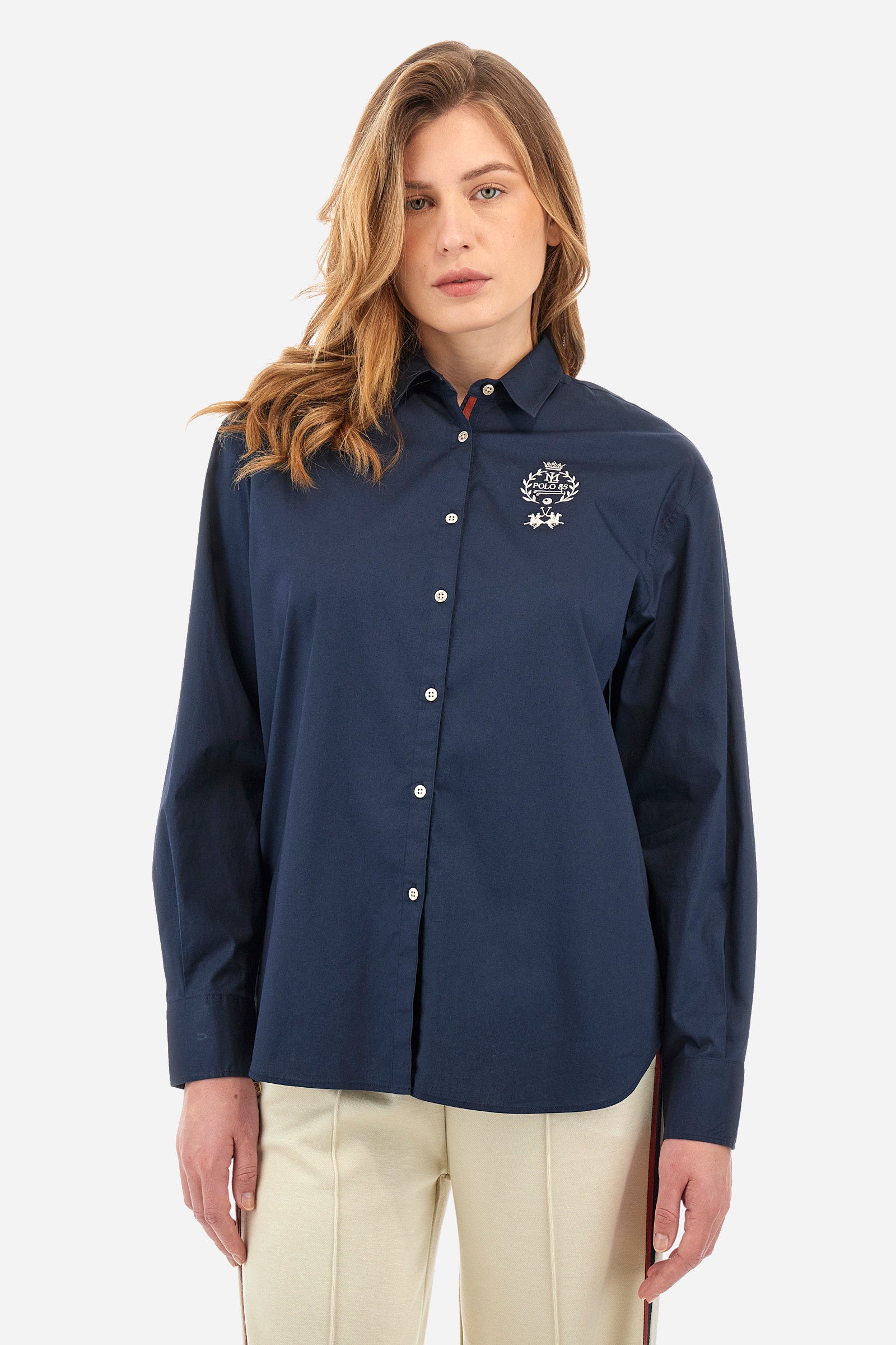 Women's long-sleeved patterned shirt in a single colour from the Polo Academy line. Made of stretch cotton. The internal part of the fastening features a touch of colour that contrasts with the main one. The logo and symbol of the Polo Academy line are sewn on the back. With buttoned cuffs. The logo is present on the back on a metal plate sewn onto a coloured strip. The fit is regular. The model wears a size 2. - Navy