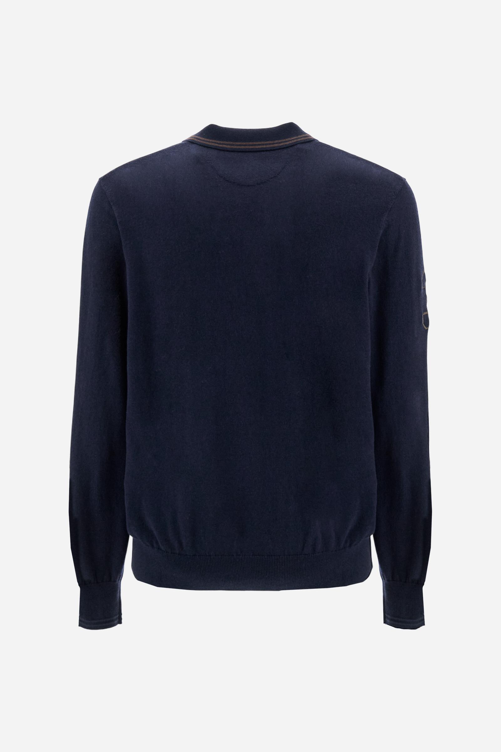 Men’s long-sleeved knitted polo in plain yarn blend (50% cotton, 50% wool), balancing comfort and warmth. Classic ribbed collar and cuffs with subtle contrasting stripe. Three personalized buttons on the placket. Small embroidered brand logo in contrasting color on the chest. On the right sleeve, a cord-embroidered number patch completes the design. Regular and slightly roomy fit. Model wears size L. - Navy