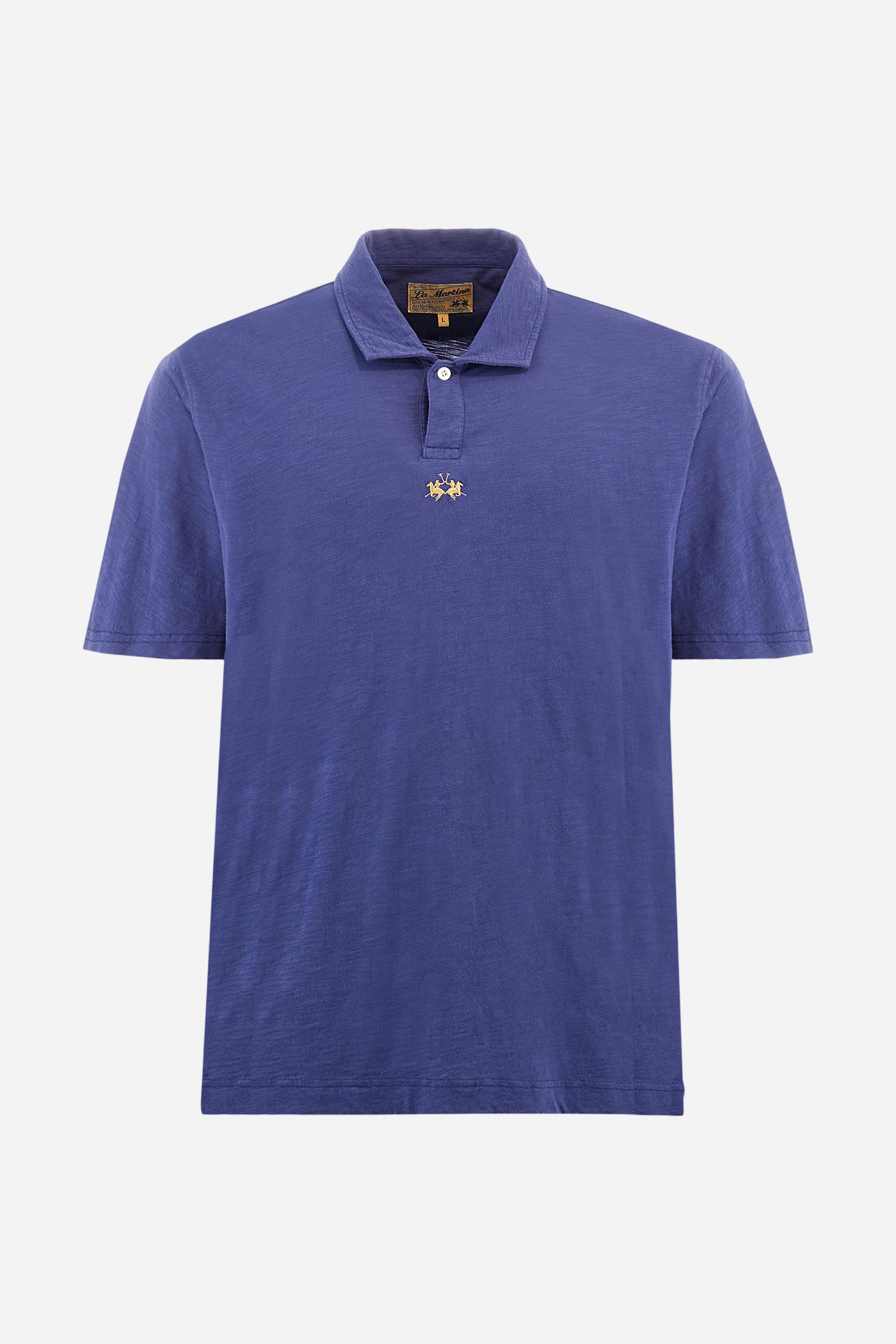 Men's short-sleeved polo shirt in a single colour, made of 100% cotton slub jersey. Fastens with a button. A fabric patch representing the garment's certificate is sewn onto the back. The logo is embroidered in contrast under the opening on the front. Comfort fit. The model is wearing a size L. - Deep Cobalt