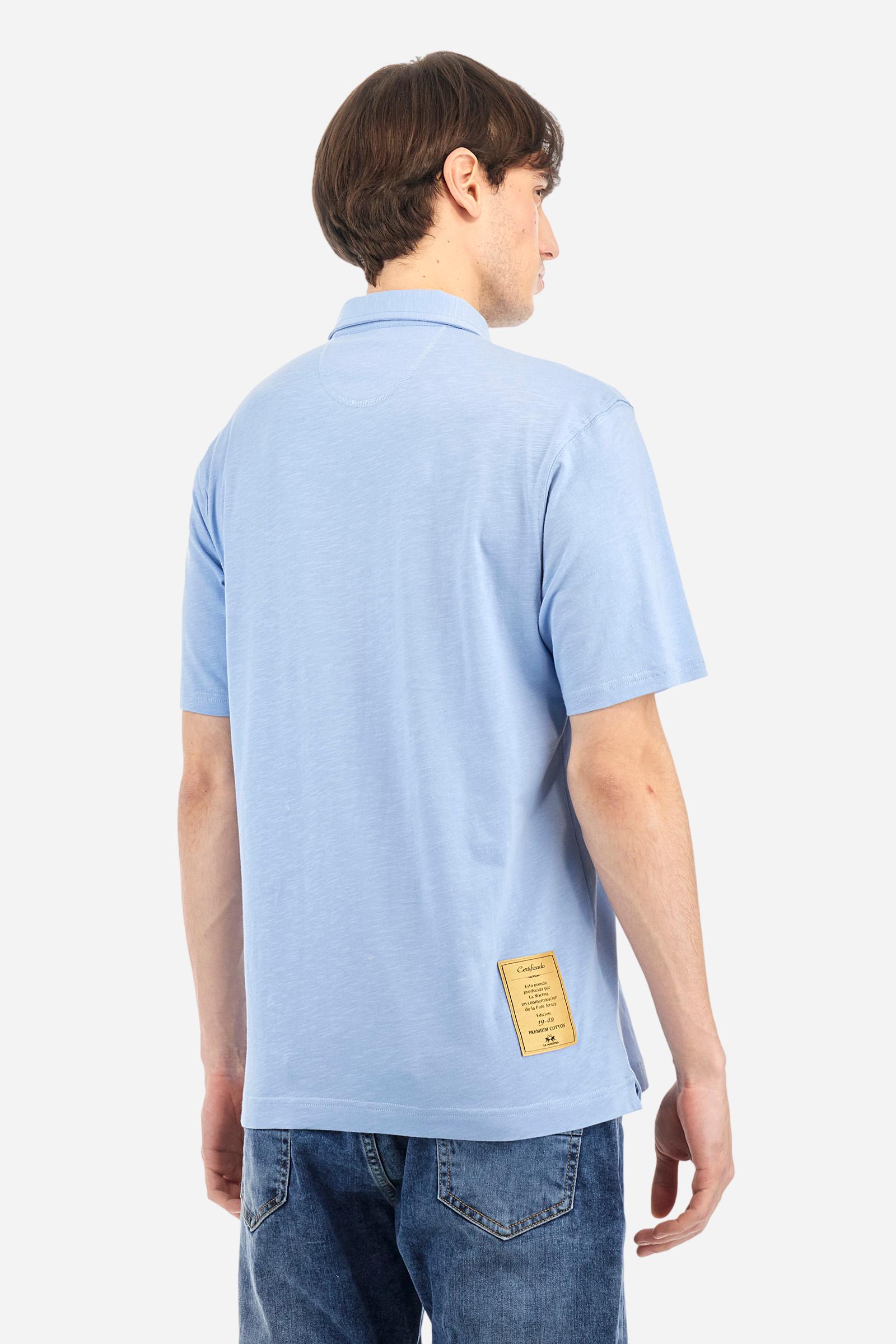 Men's short-sleeved polo shirt in a single colour, made of 100% cotton slub jersey. Fastens with a button. A fabric patch representing the garment's certificate is sewn onto the back. The logo is embroidered in contrast under the opening on the front. Comfort fit. The model is wearing a size L. - Vista Blue
