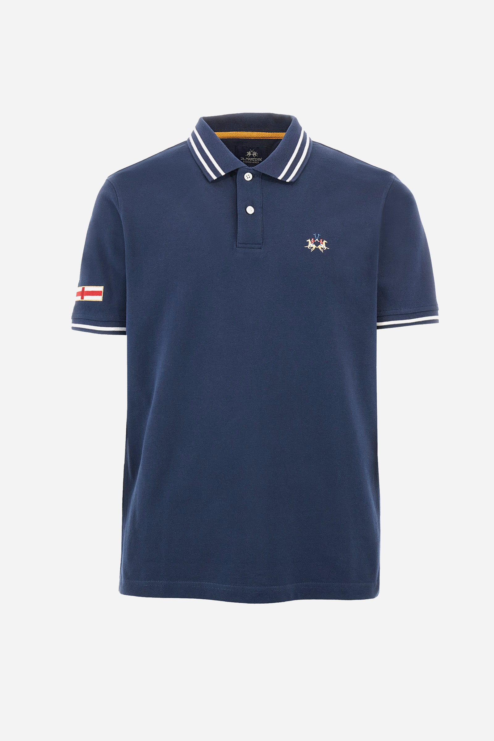 Men’s polo shirt in solid color with short sleeves in 100% cotton piquet. Two button closure. Edge and inner neck, along with the armhole all profiled with contrasting stripes. On one of the sleeves is applied a patch depicting the flag of the country to recall the capsule collection Ciudades. Small La Martina logo embroidered on the chest. The fit is regular. The model wears a size L. - Navy