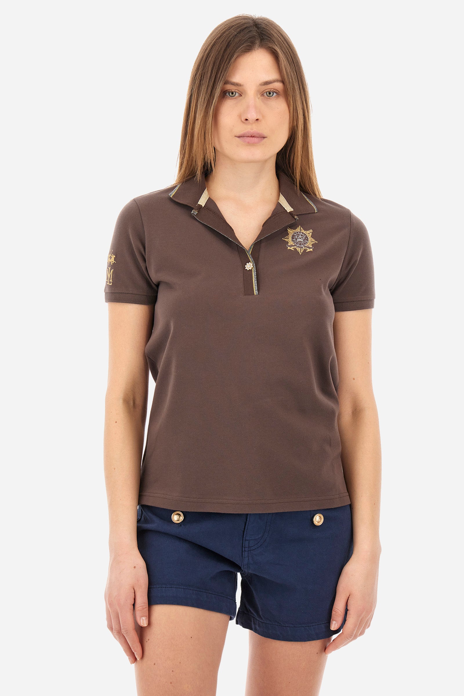 Women’s polo with short sleeves in solid color. Made of stretch cotton. V-neck and jewel button closure. Ribbed crew neck and armhole, both profiled by a lamé strip. The under collar embellished with a different color print along with mini logo and symbol on the chest and sleeve are characteristic of the capsule Guards. The fit is regular. The model wears a size 2. - French Roast