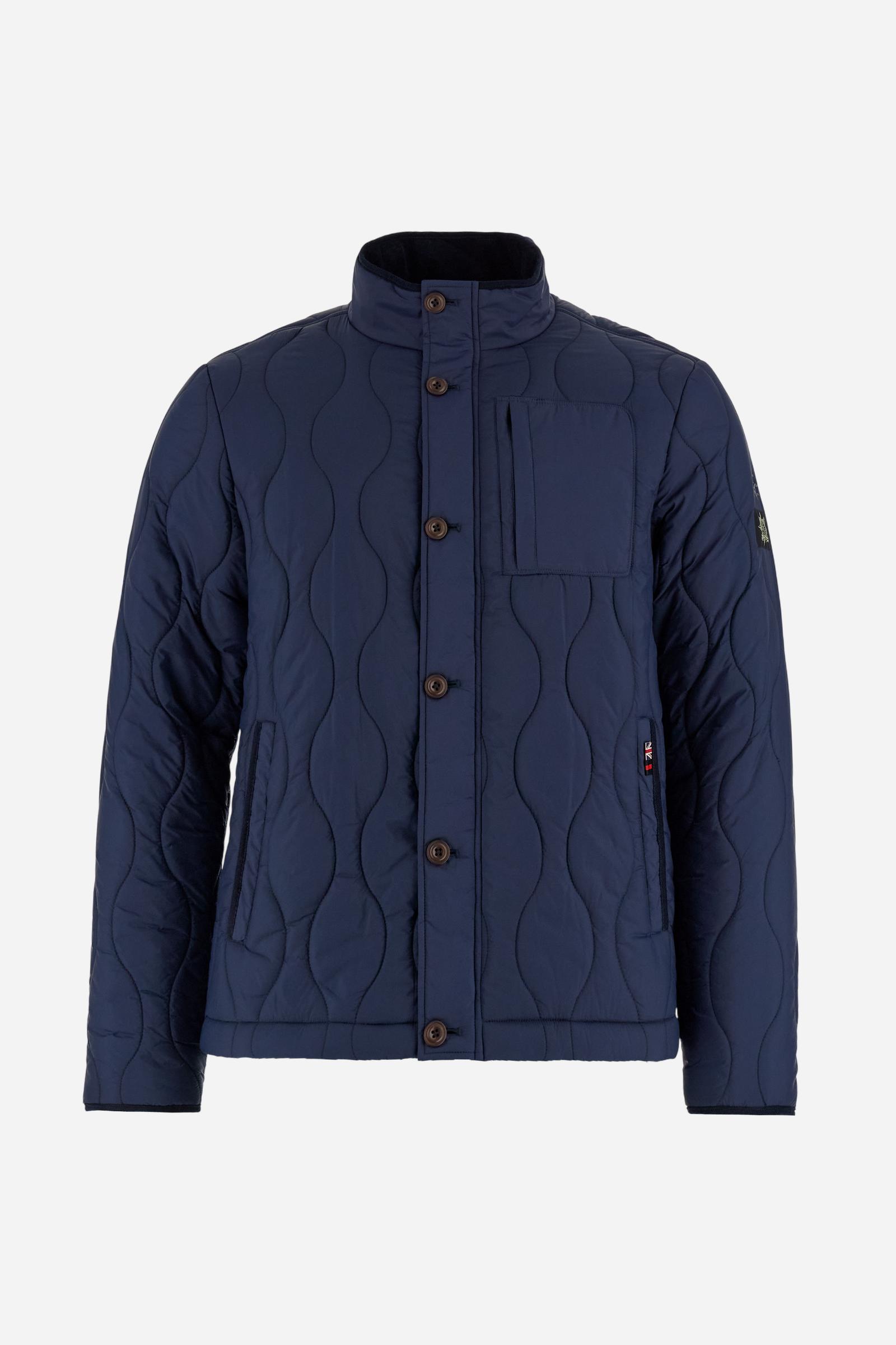 Men’s quilted nylon husky jacket with high collar. Front closure with customized zip and large faux-leather buttons. Interior lined with striped bicolor polyester. Contrast details on the inside (pockets, profiles, back-neck tab). Clean design with chest pocket closed by zip and vertical side pockets. Adjustable back straps with metal snap buttons. Logo patches on the sleeves and multicolor embroidered lettering on the outer collar. Part of the Guards capsule. Regular fit. Model wears size L. - Navy