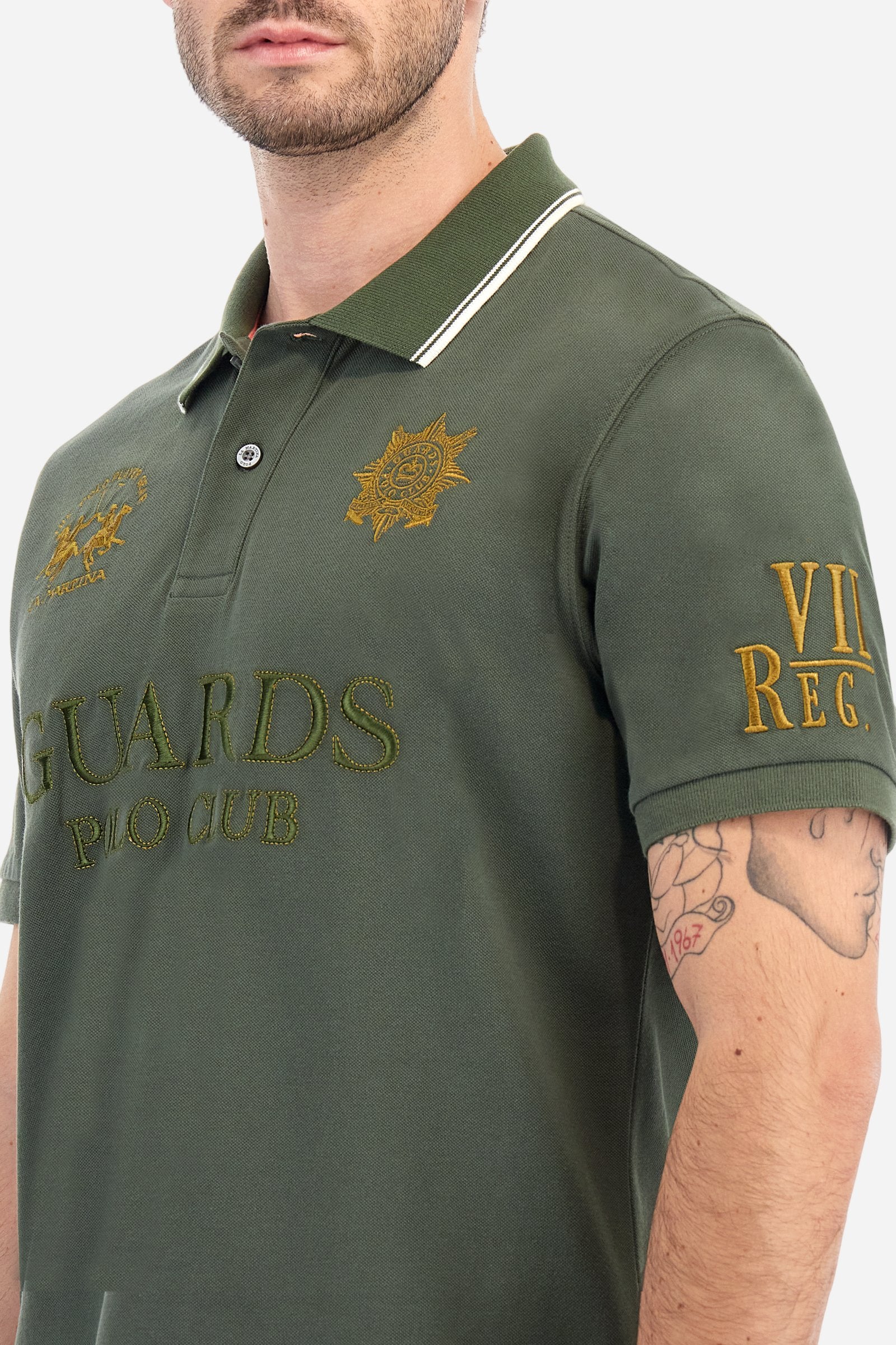 Men's short-sleeved Guards polo shirt in a single colour, made of cotton piqué. Fastens with two buttons. The collar is ribbed with striped trim in a contrasting colour. The graphics on the chest and sleeves are all made using the embroidery technique. The central lettering on the chest is a 3D embroidery in the same colour as the base fabric. The large colour-contrasting logo is embroidered on the chest. The fit is regular. The model is wearing a size L. - Thyme