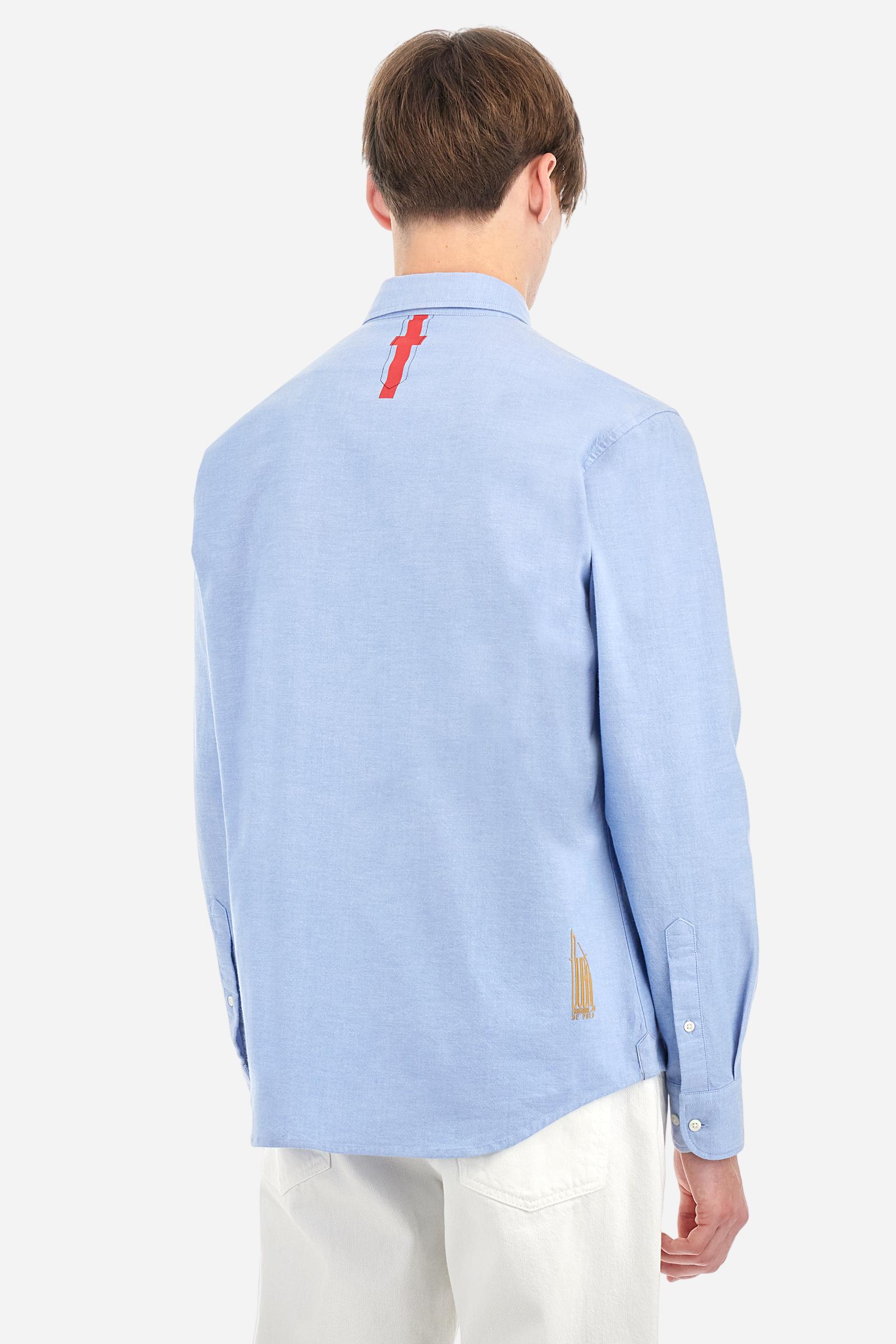 Men's long-sleeved plain shirt made from 100% Oxford cotton. The button-down collar is finished with a second button printed with the English flag. The multicoloured embroidery on the chest, over the heart, includes lettering, numbers and the logo, which add a distinctive touch. Regular fit. The model is wearing a size L. - Cornflower blue