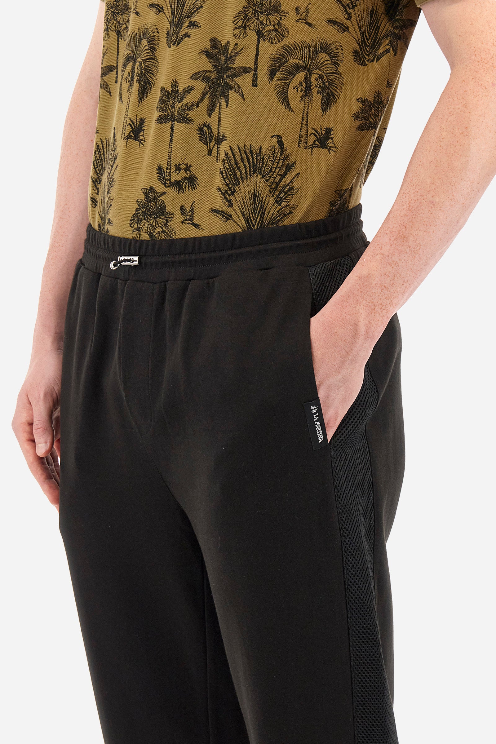 Men's single-colour jogging bottoms in mixed cotton. Drawstring at the waist and double welt pocket on the front. Featuring a side stripe with a honeycomb texture. On the back there is a single open pocket featuring the brand's initials. The fit is regular. The model wears a size L. - Black