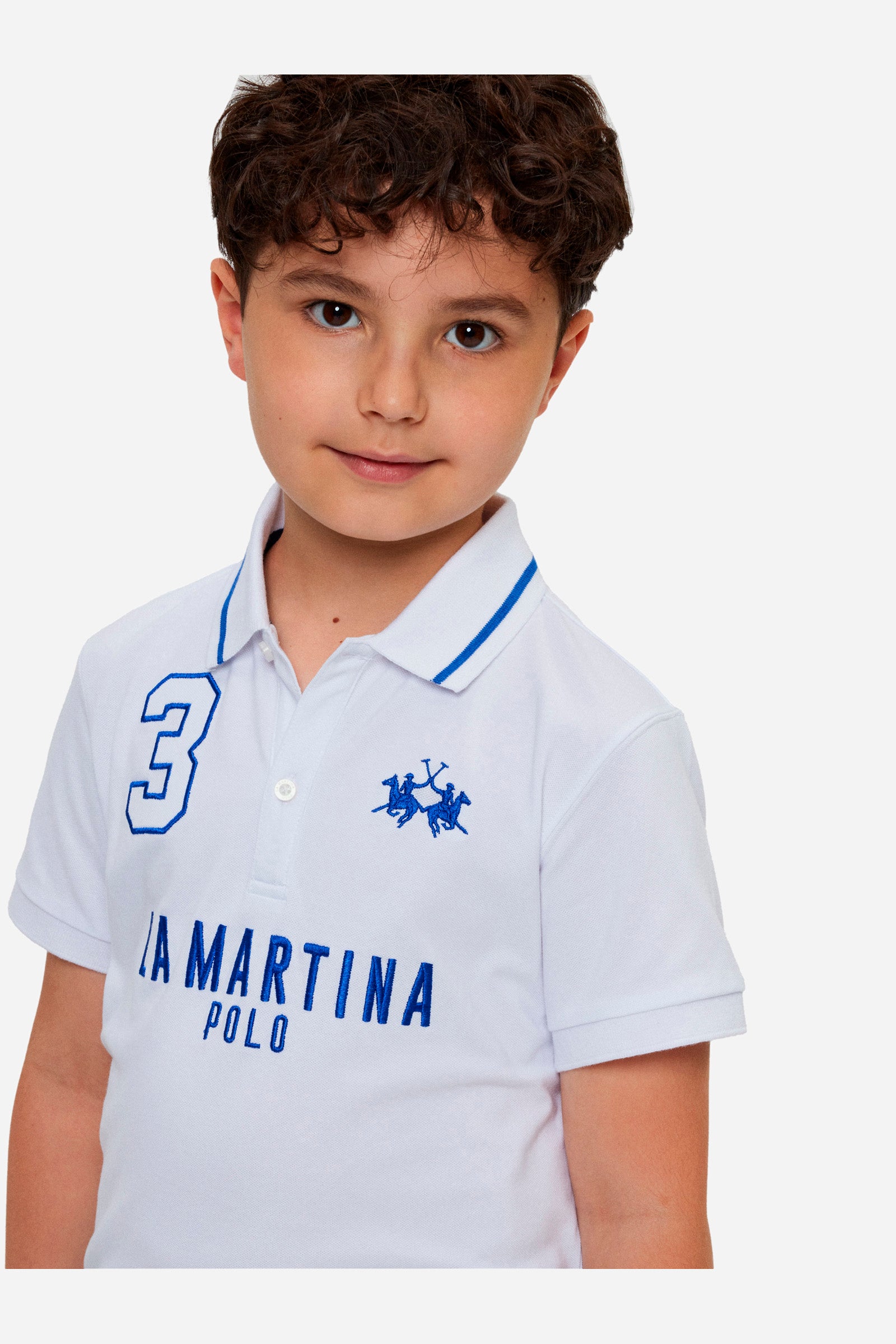 Boys' single-colour polo shirt made of pique cotton. Profiled collar, with contrasting colour thread. Fastens with two buttons. Also featuring embroidered lettering in contrasting colours on the front. The logo is embroidered on the chest, left side. - Optic White/Blue