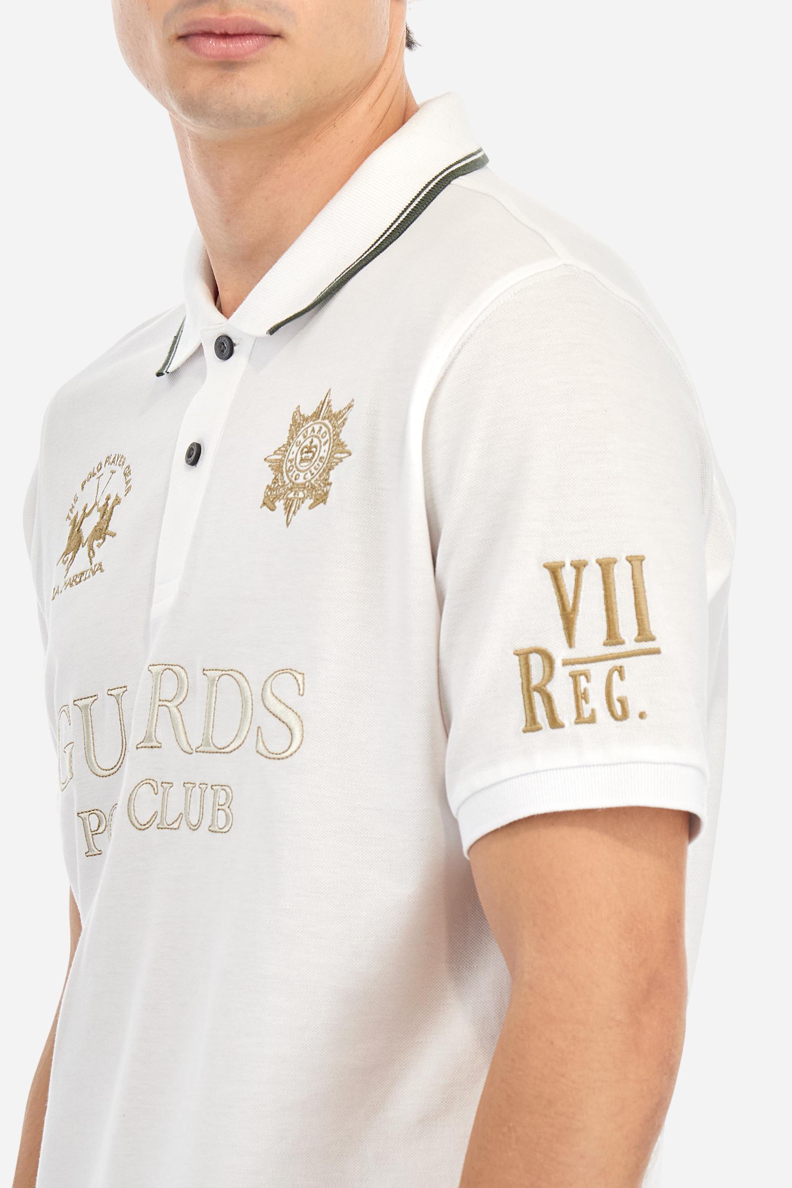 Men's short-sleeved Guards polo shirt in a single colour, made of cotton piqué. Fastens with two buttons. The collar is ribbed with striped trim in a contrasting colour. The graphics on the chest and sleeves are all made using the embroidery technique. The central lettering on the chest is a 3D embroidery in the same colour as the base fabric. The large colour-contrasting logo is embroidered on the chest. The fit is regular. The model is wearing a size L. - Optic White