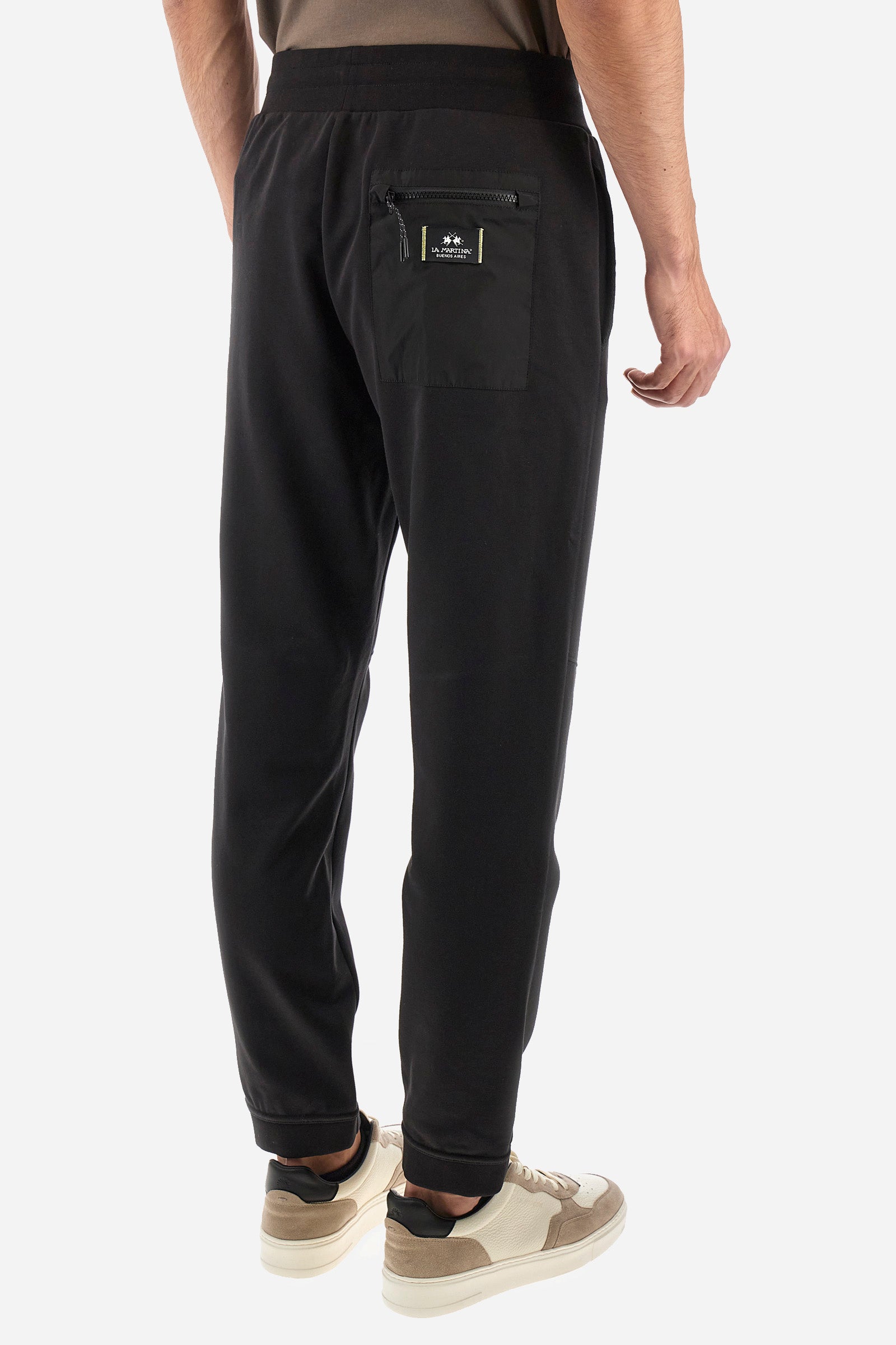 Men's single-colour jogging bottoms in a cotton sweat fabric. With a drawstring waist and double front pocket. With different shades at the bottom of the leg. On the back there is a pocket with a zip fastening featuring contrasting textures and colours. The logo is present on the tag sewn on the back pocket. The fit is regular. The model wears a size L. - Black