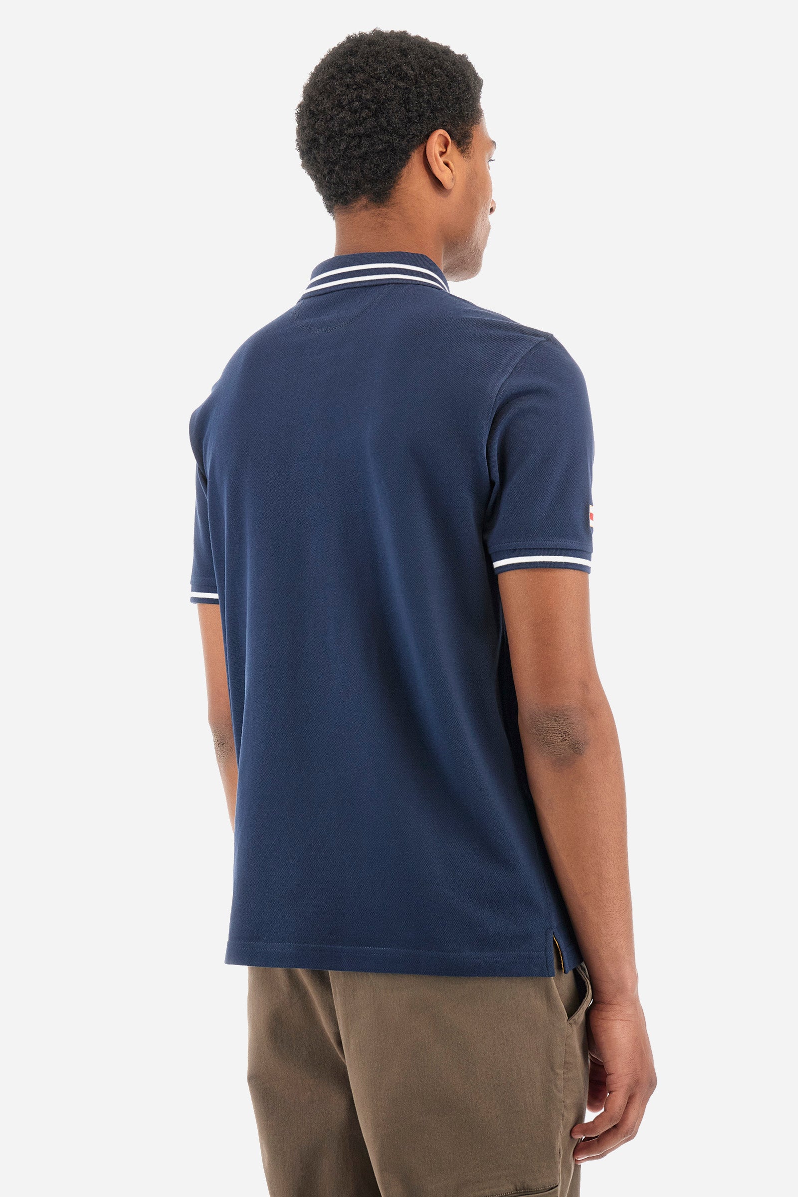 Men’s polo shirt in solid color with short sleeves in 100% cotton piquet. Two button closure. Edge and inner neck, along with the armhole all profiled with contrasting stripes. On one of the sleeves is applied a patch depicting the flag of the country to recall the capsule collection Ciudades. Small La Martina logo embroidered on the chest. The fit is regular. The model wears a size L. - Navy
