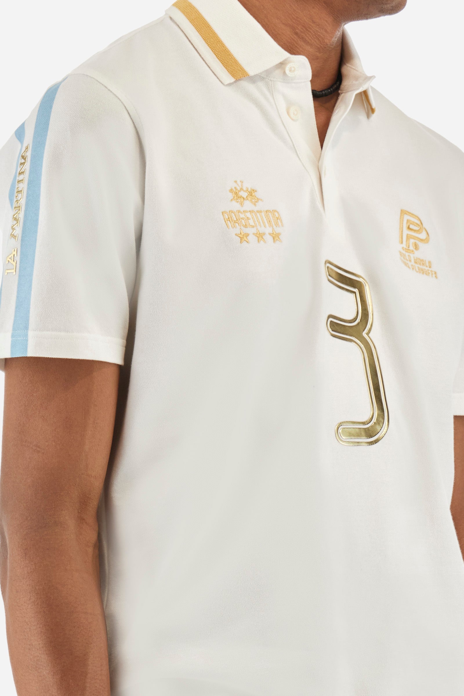 Men's single-colour short-sleeved polo in elasticated cotton. Three-button fastening. Collar with contrasting colour stripe. The front features embroidered lettering, the number 3, the word "Argentina", and a small logo. On one sleeve we find the "La Martina" lettering with two stripes in the colours of the Argentinian flag. The back features additional "Argentina" lettering, a print of the number 3, and symbols representing the nation. The fit is regular. The model wears a size L. - Optic White