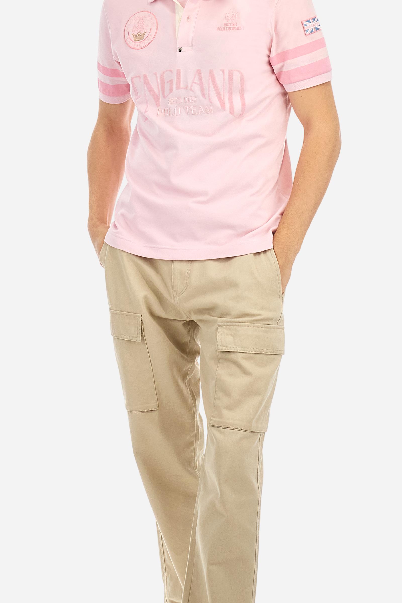 Short-sleeved, single-colour men's polo shirt made of stretch cotton piqué. Fastens with two buttons. Sleeve details in fabric with colour-contrasting irregular band pattern. Ribbed collar with brand name embroidery in contrasting colour. The front graphics are embroidered, the large central lettering is a flocked transfer, while the flag on the sleeve is an applied patch. The logo is embroidered on the chest, left side. The fit is regular. The model is wearing a size L. - Parfait Pink