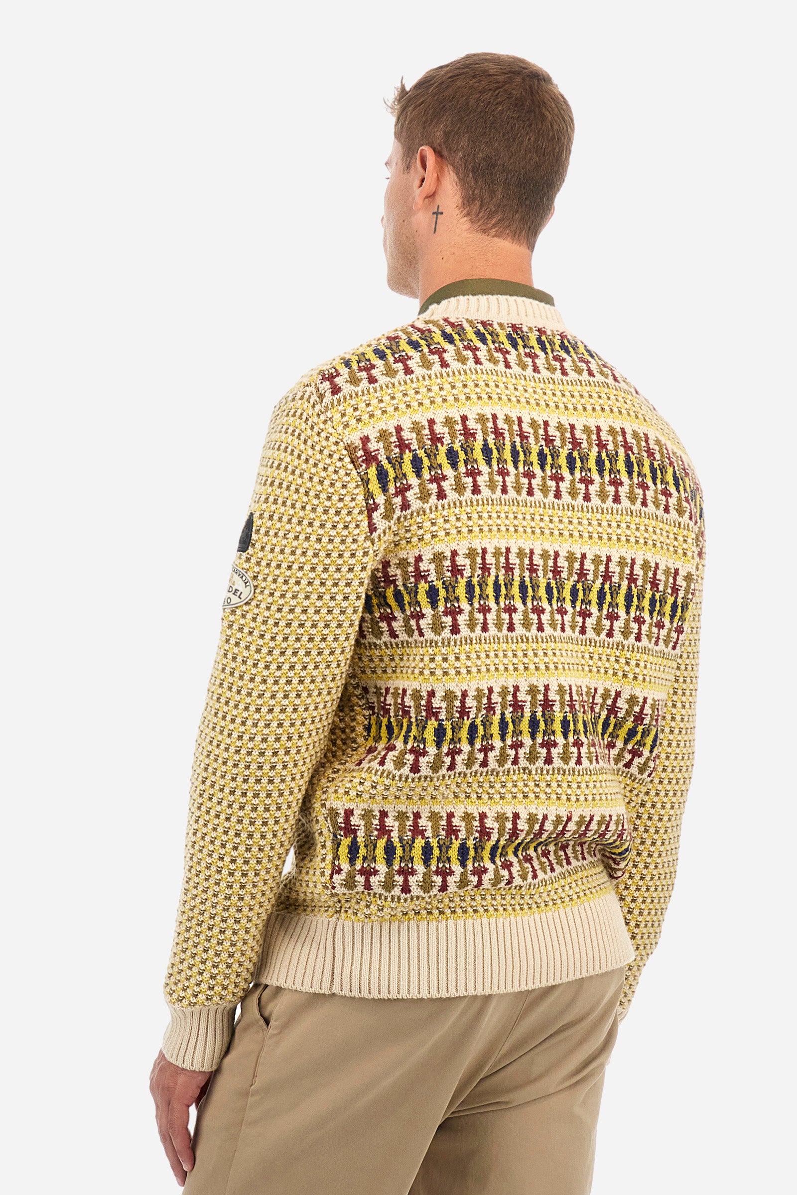 Men's crewneck pullover with long sleeves, made from a wool-blend yarn. The jacquard pattern differs on the front and sleeves, featuring a micro-check effect, while the back showcases a larger pattern with horizontal blocks. The collar, hem, and cuffs are in solid ribbed fabric. A patch inspired by Tierra del Fuego and a rubberized logo patch are applied on the sleeve. The fit is comfortable. - Jacquard Multicolour