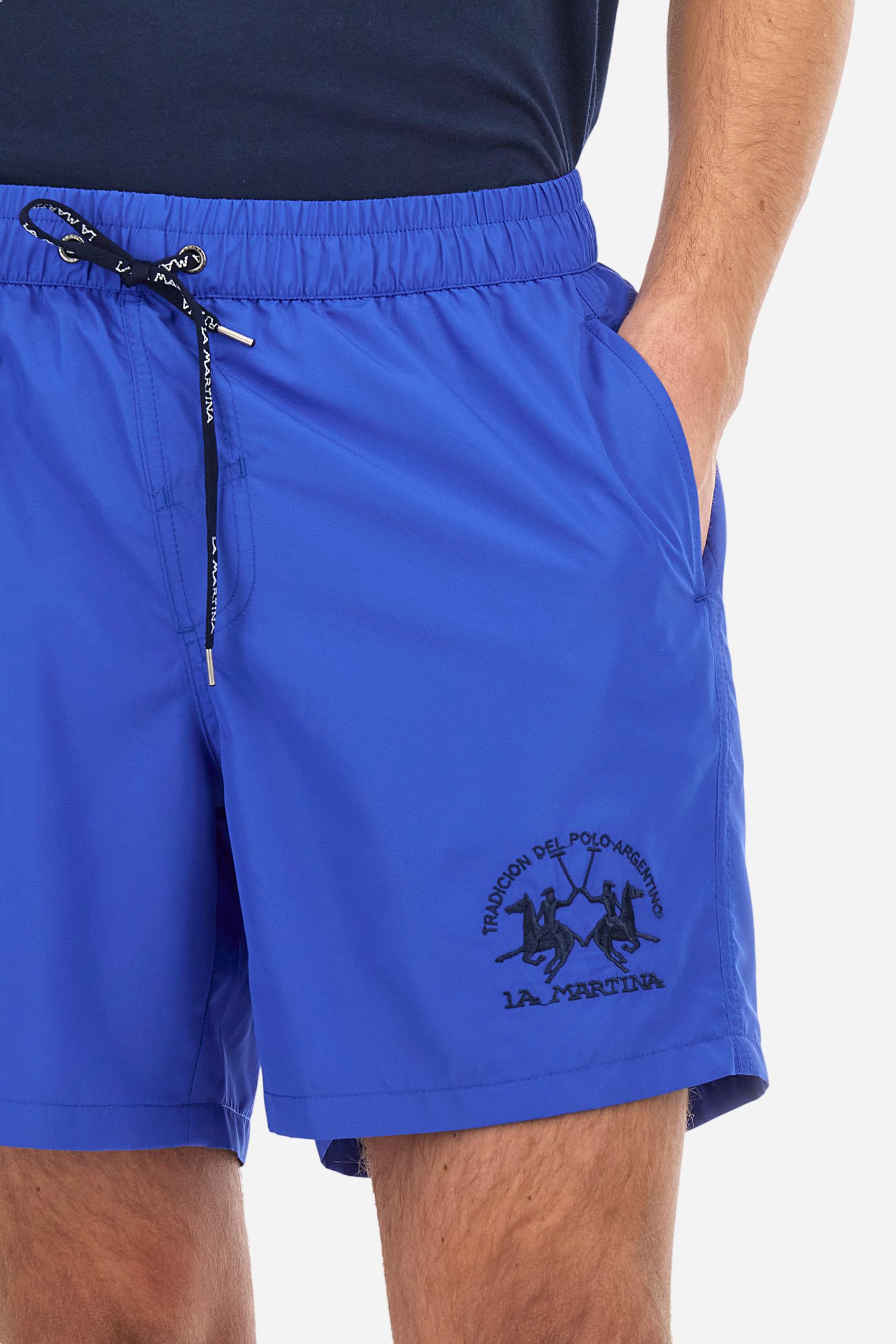 Plain men's swimming shorts made of nylon. Elastic waistband with a personalised drawstring for waist adjustment. On the inside of the shorts is an elasticated mesh brief. Double side pocket on the hips and patch pocket with flap on the back, on the right side only. The large logo is embroidered in a contrasting colour thread on the bottom of the left leg on the front. Regular fit. The model is wearing a size L. - Dazzling Blue