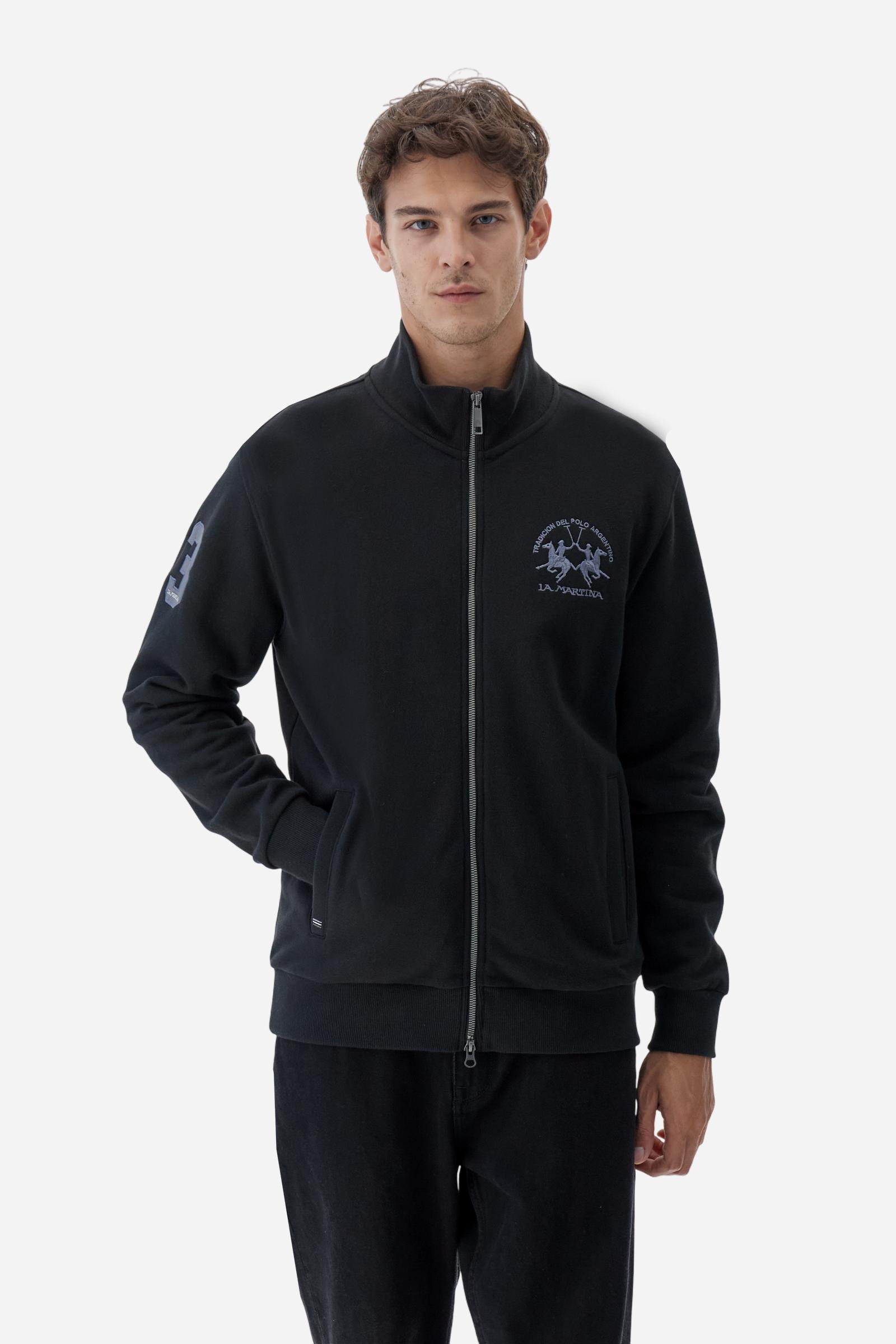 Men's long-sleeved solid colour sweatshirt. It is made of comfortable 100% cotton fleece with a soft-brushed feel. Model with high ribbed neck and front zip opening. Solid colour ribbed cuffs and waistband. The large contrasting brand team logo is embroidered on the chest. A contrasting colour fabric number patch is applied to the right sleeve. The model has a regular fit that offers a comfortable, relaxed silhouette. The model is wearing a size L. - Black