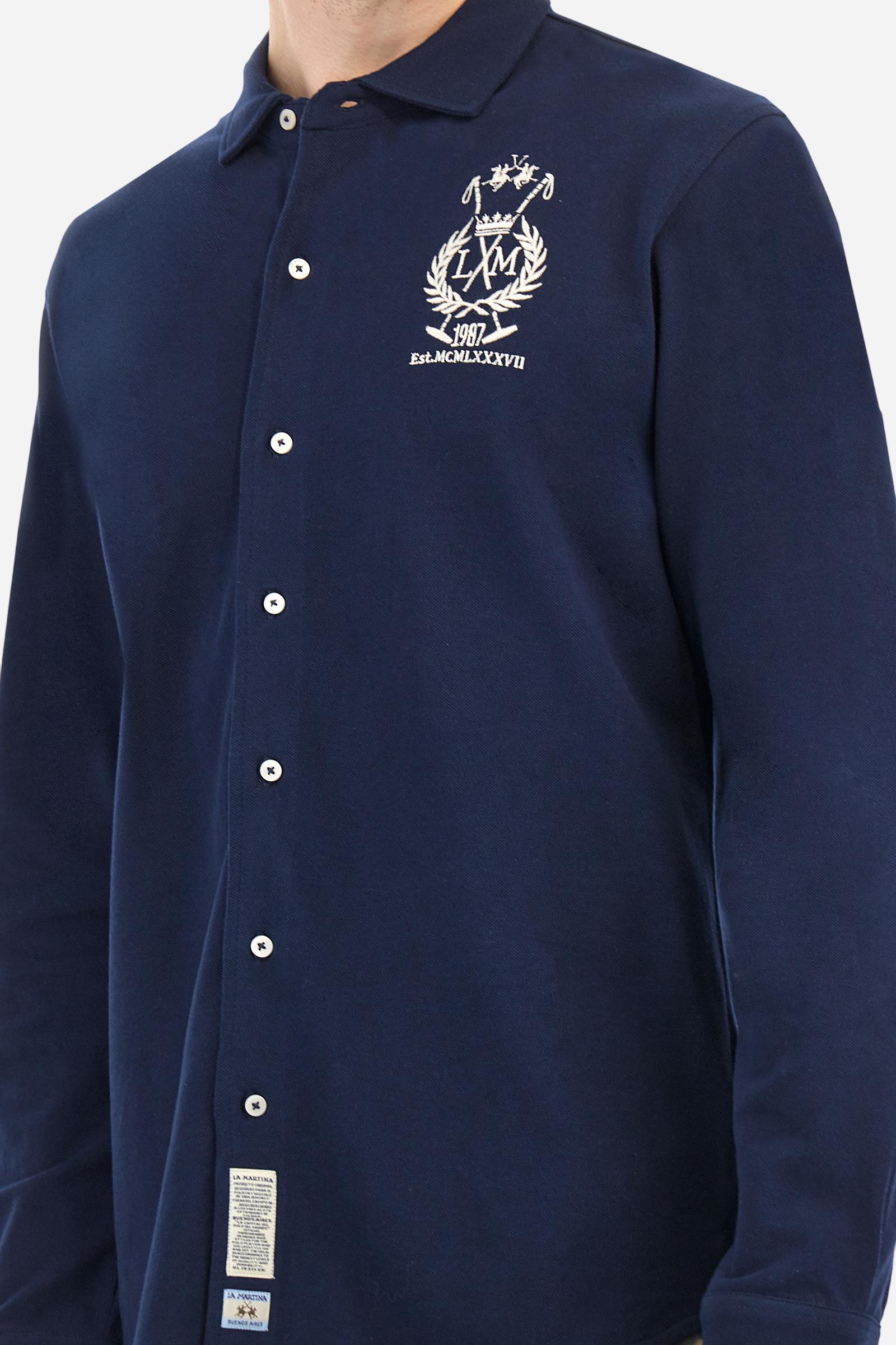 Men's plain long-sleeved shirt made from cotton piqué. It features an elegant spread collar and a seamless front opening, with no visible stitching. A graphic is embroidered on the chest, over the heart, in contrasting thread. Regular fit. The model is wearing a size L. - Navy