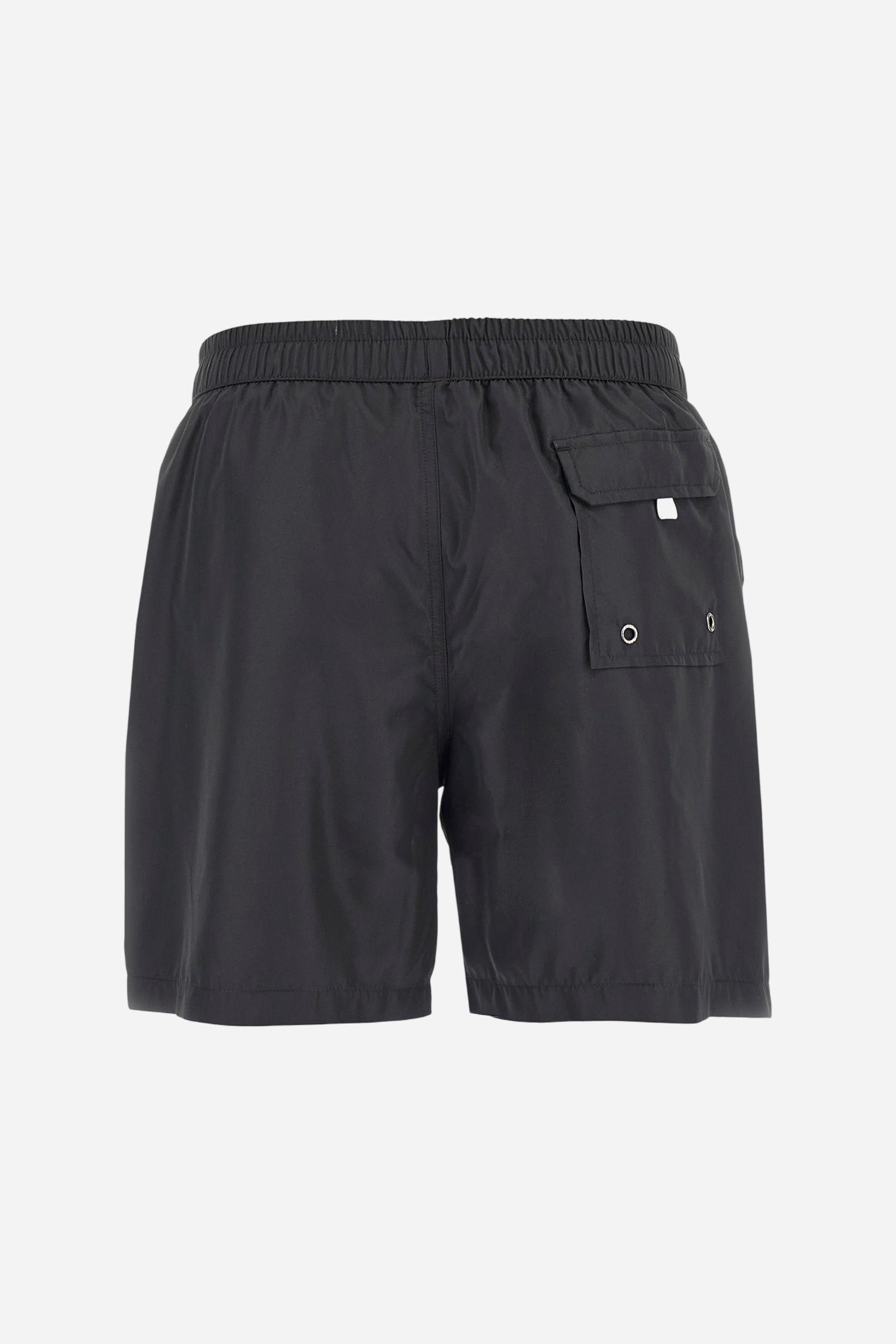 Plain men's swimming shorts made of nylon. Elastic waistband with a personalised drawstring for waist adjustment. On the inside of the shorts is an elasticated mesh brief. Double side pocket on the hips and patch pocket with flap on the back, on the right side only. The large logo is embroidered in a contrasting colour thread on the bottom of the left leg on the front. Regular fit. The model is wearing a size L. - Black