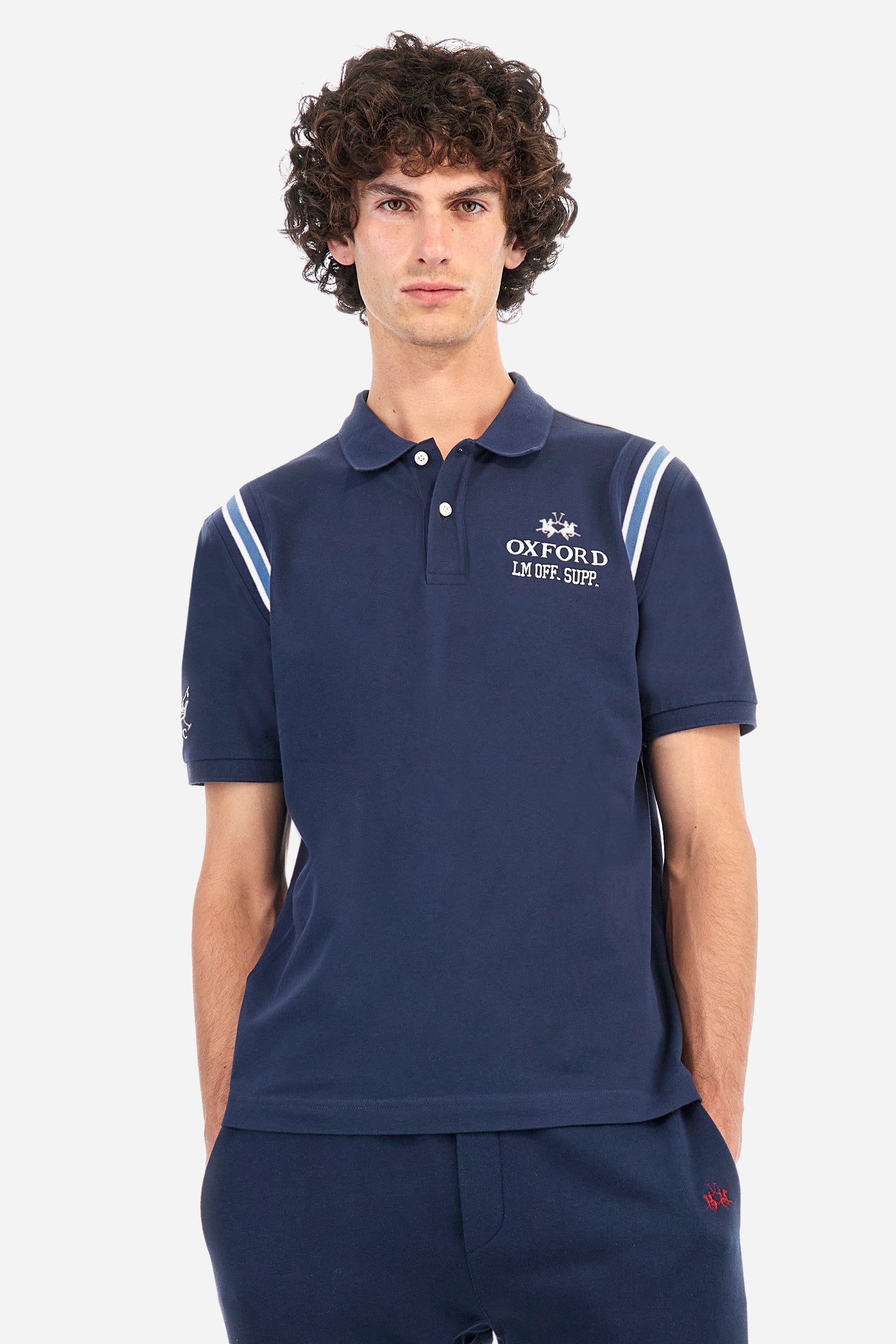 Men's short-sleeved polo shirt in plain stretch cotton. Two-button fastening. The sleeves are finished with contrasting stripes. The logo and lettering associated with the Oxford line are embroidered on the front. Regular fit. The model is wearing a size L. - Navy