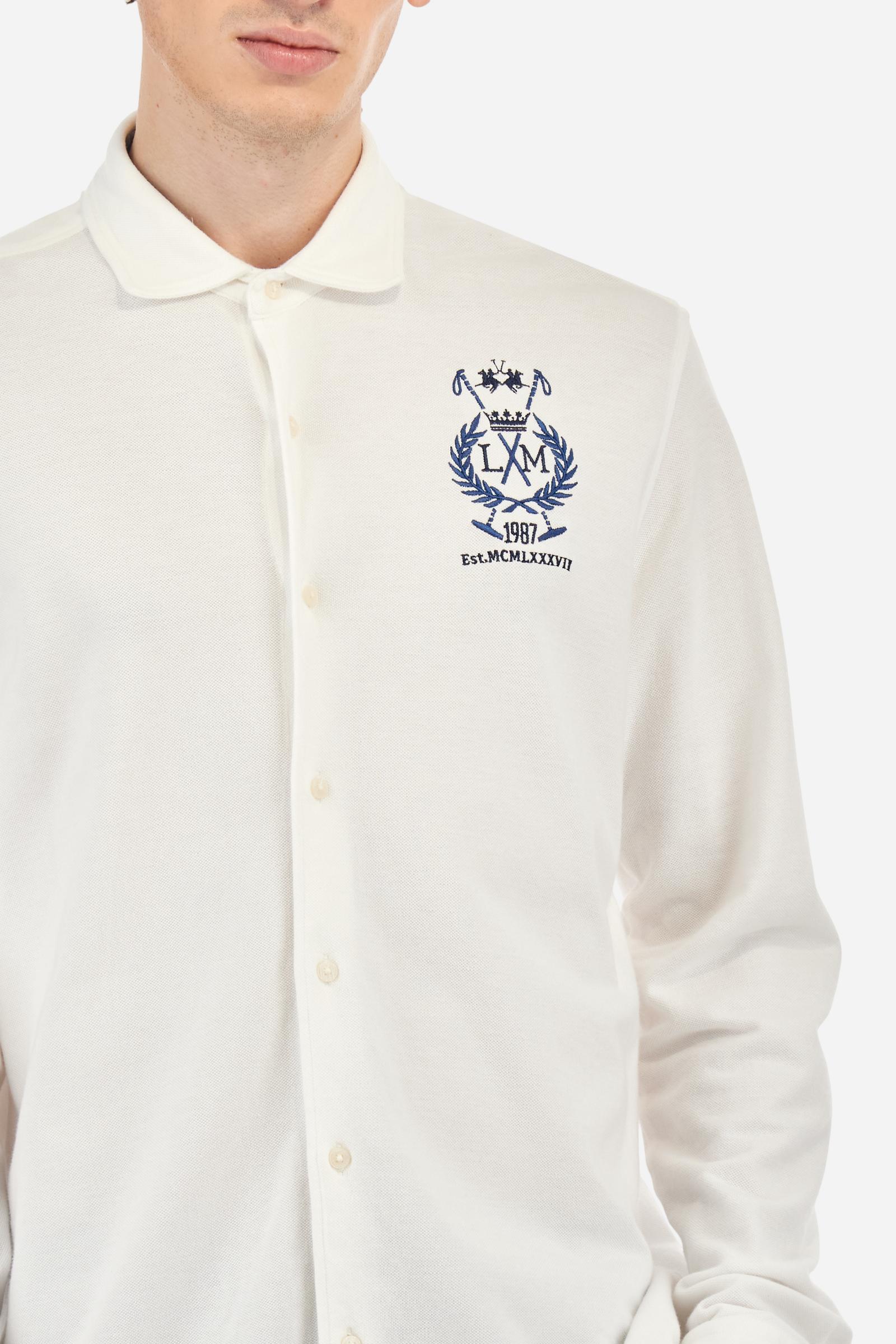 Men's plain long-sleeved shirt made from cotton piqué. It features an elegant spread collar and a seamless front opening, with no visible stitching. A graphic is embroidered on the chest, over the heart, in contrasting thread. Regular fit. The model is wearing a size L. - Optic White