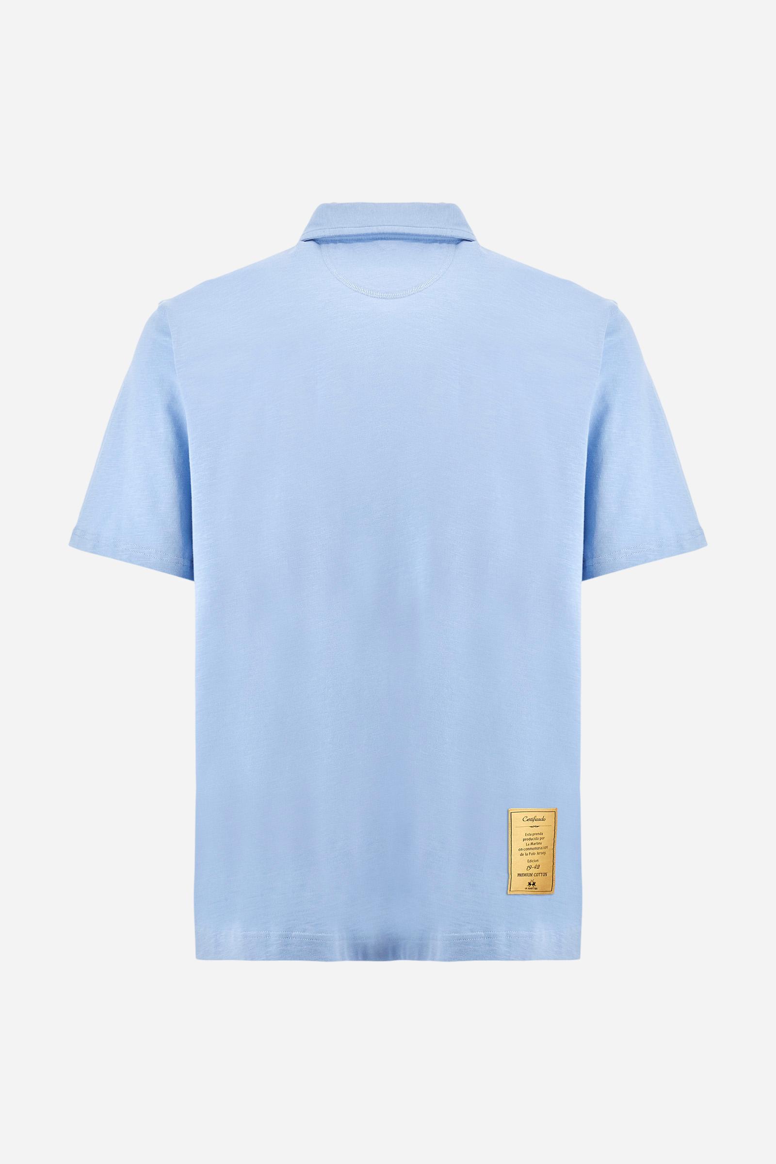 Men's short-sleeved polo shirt in a single colour, made of 100% cotton slub jersey. Fastens with a button. A fabric patch representing the garment's certificate is sewn onto the back. The logo is embroidered in contrast under the opening on the front. Comfort fit. The model is wearing a size L. - Vista Blue