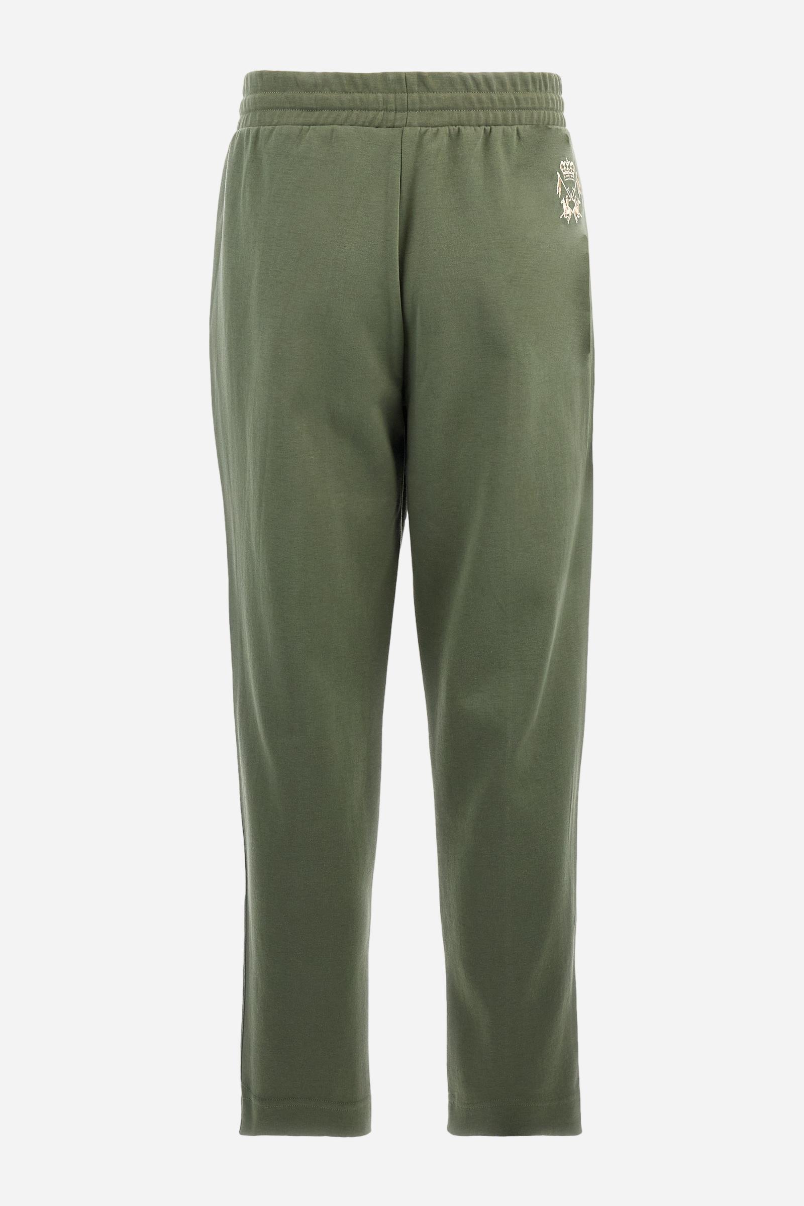 Single-colour men's jogging trousers made of lightweight cotton-blend interlock fleece. Drawstring waistband. Side pockets with matching zip fastening. On both sides, there are multicoloured striped jersey bands. The front features vertical ribbed detailing. The logo is embroidered in colour-contrasting thread on the back, under the strap, towards the right side. Regular fit. The model is wearing a size L. - Thyme