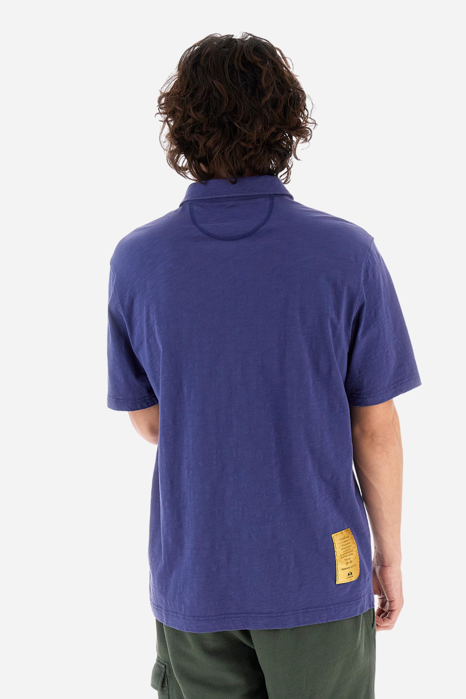 Men's short-sleeved polo shirt in a single colour, made of 100% cotton slub jersey. Fastens with a button. A fabric patch representing the garment's certificate is sewn onto the back. The logo is embroidered in contrast under the opening on the front. Comfort fit. The model is wearing a size L. - Deep Cobalt