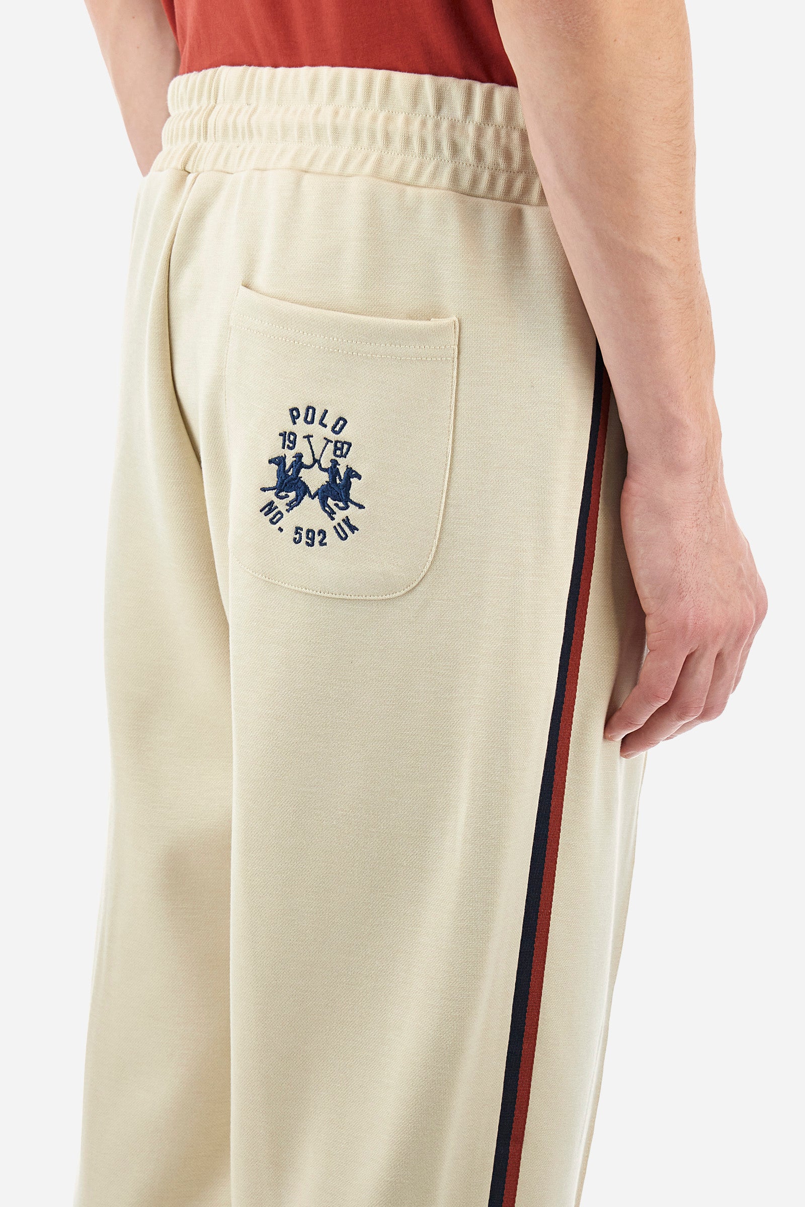 Men's single-colour jogging bottoms in a sweat fabric from the Polo Academy line, with contrasting details. Made of synthetic material. Drawstring waist. Double back pocket with contrasting zip fastening. Another pocket is present on the back. With coloured stripes on the sides of the trousers. The logo is sewn on the back pocket. The fit is regular. The model wears a size L. - Bone White