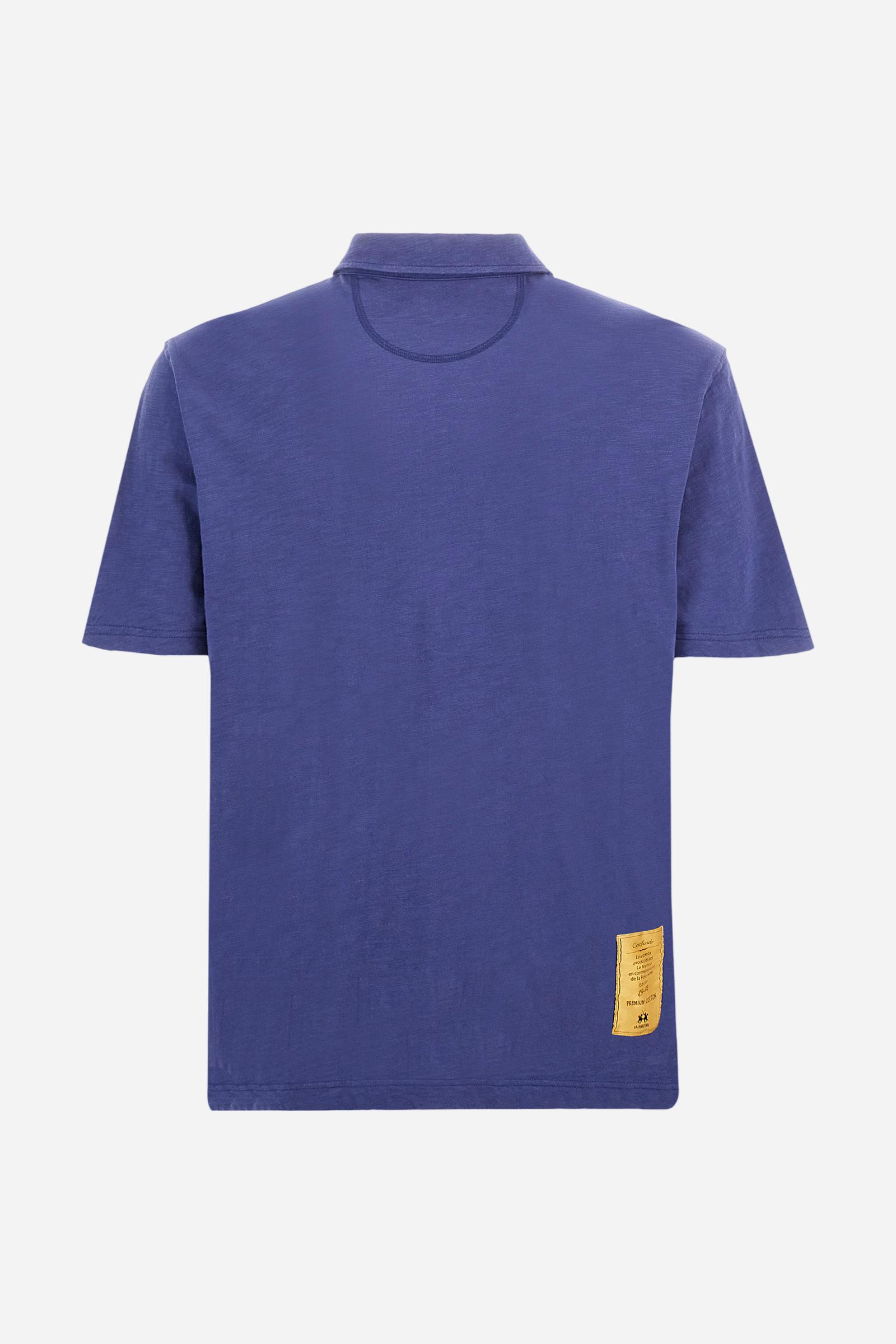 Men's short-sleeved polo shirt in a single colour, made of 100% cotton slub jersey. Fastens with a button. A fabric patch representing the garment's certificate is sewn onto the back. The logo is embroidered in contrast under the opening on the front. Comfort fit. The model is wearing a size L. - Deep Cobalt