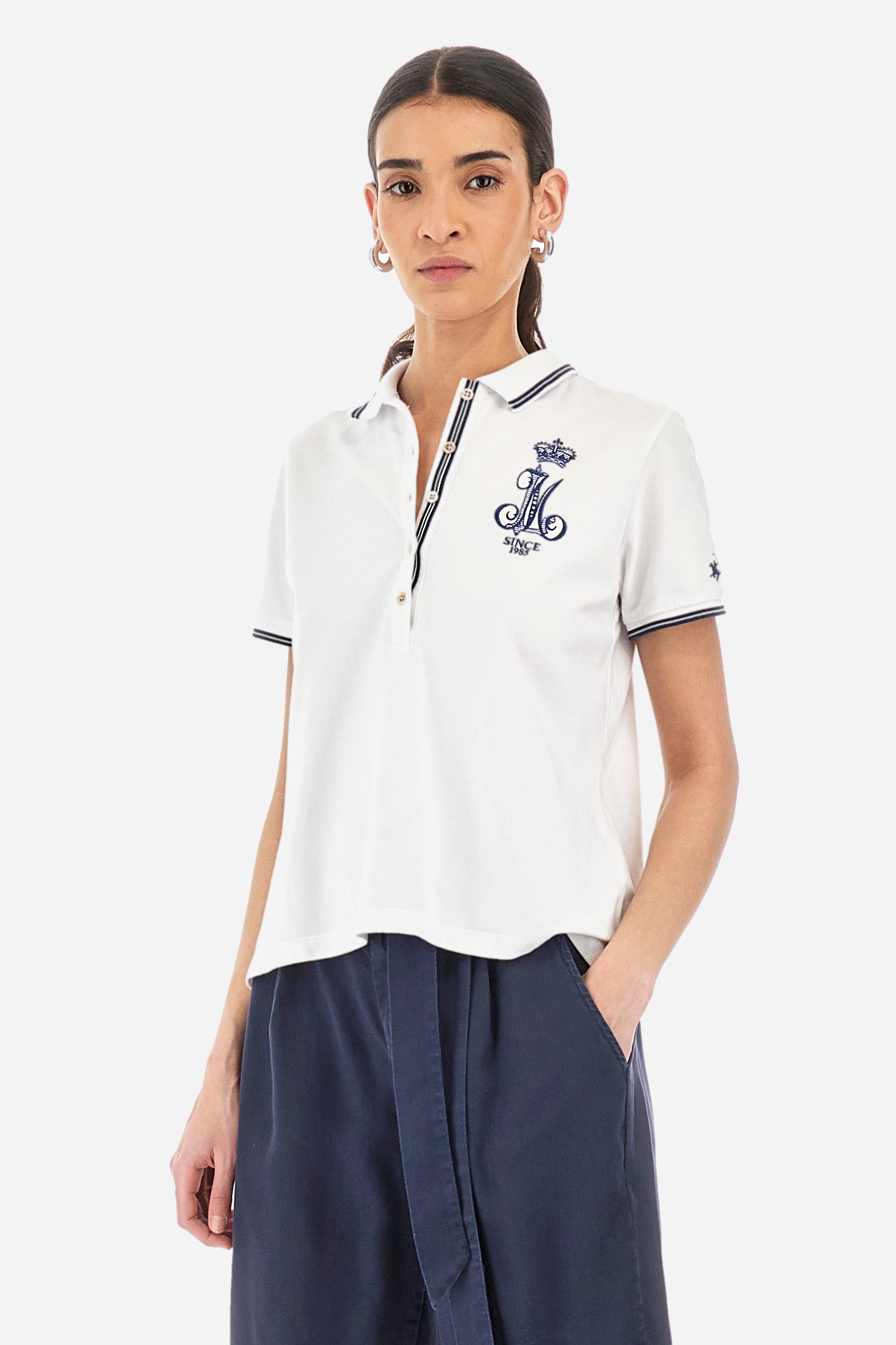 Women’s polo with short sleeves in solid color, made of stretch cotton. 5-button closure, ribbed collar and crew sleeves, where contrasting stripes are sewn. Side slits. On the front are embroideries with symbols and initials of the brand, recalling the capsule collection Polo Club Grand Hotel. The logo is embroidered on a contrasting sleeve. The fit is regular. The model wears a size 2. - Optic White