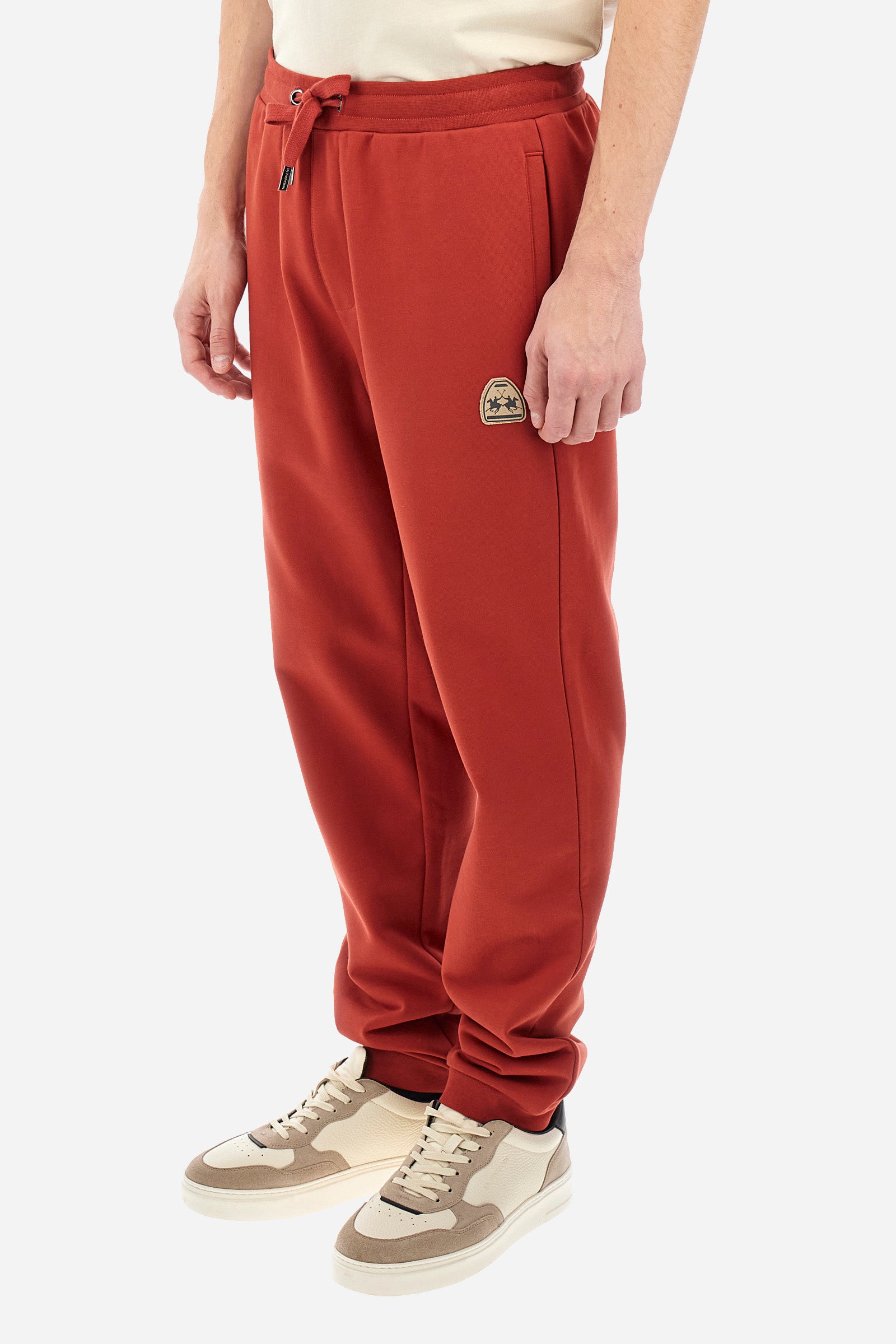 Men's single-colour jogging bottoms in a cotton sweat fabric from the Polo Academy line. With a drawstring waist and double front pocket. Another pocket is present on the back. The logo is present on a patch applied under one of the front pockets. The fit is regular. The model wears a size L. - Cinnabar