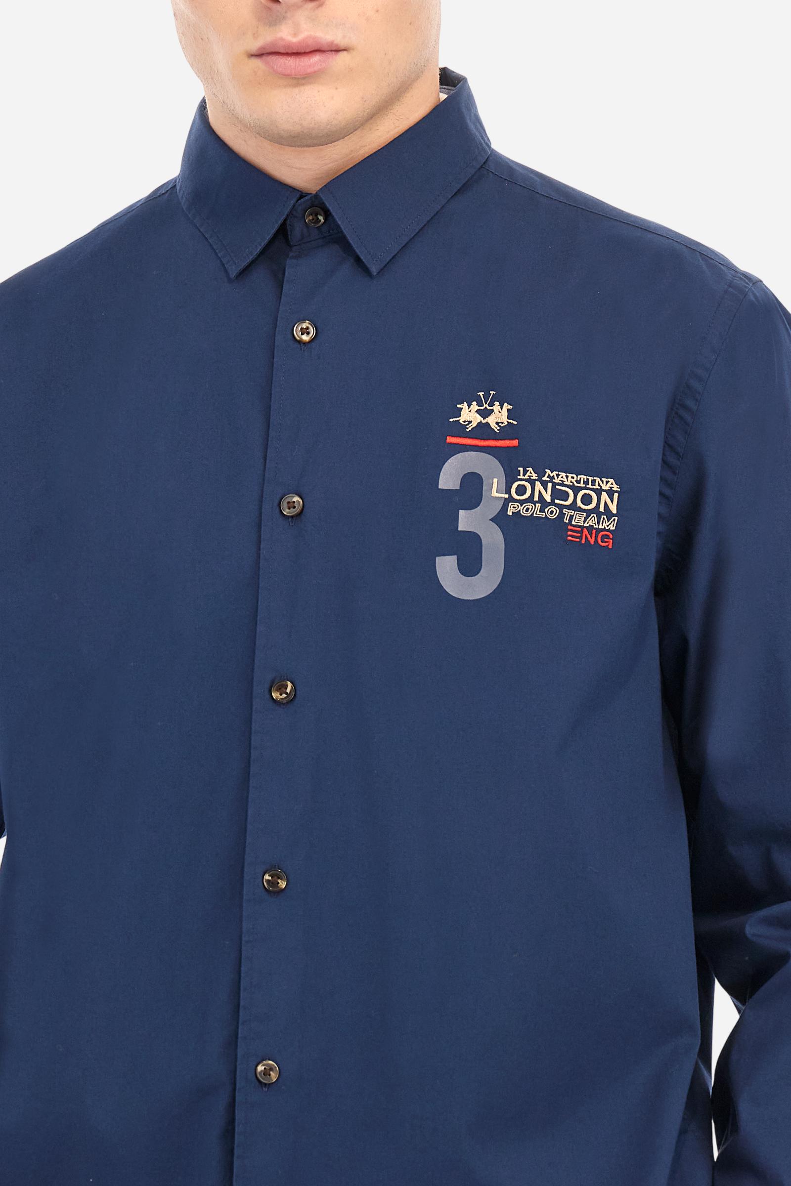 Men's single-colour long-sleeved shirt, made from 100% cotton poplin. Spread collar. Contrasting printed fabric details on the inside of the collar and opening. The numbers on the chest and back graphics are rubberised prints, while the rest of the graphics are embroidered. The logo and La Martina lettering is embroidered on the left chest. The fit is regular. The model is wearing a size L. - Navy