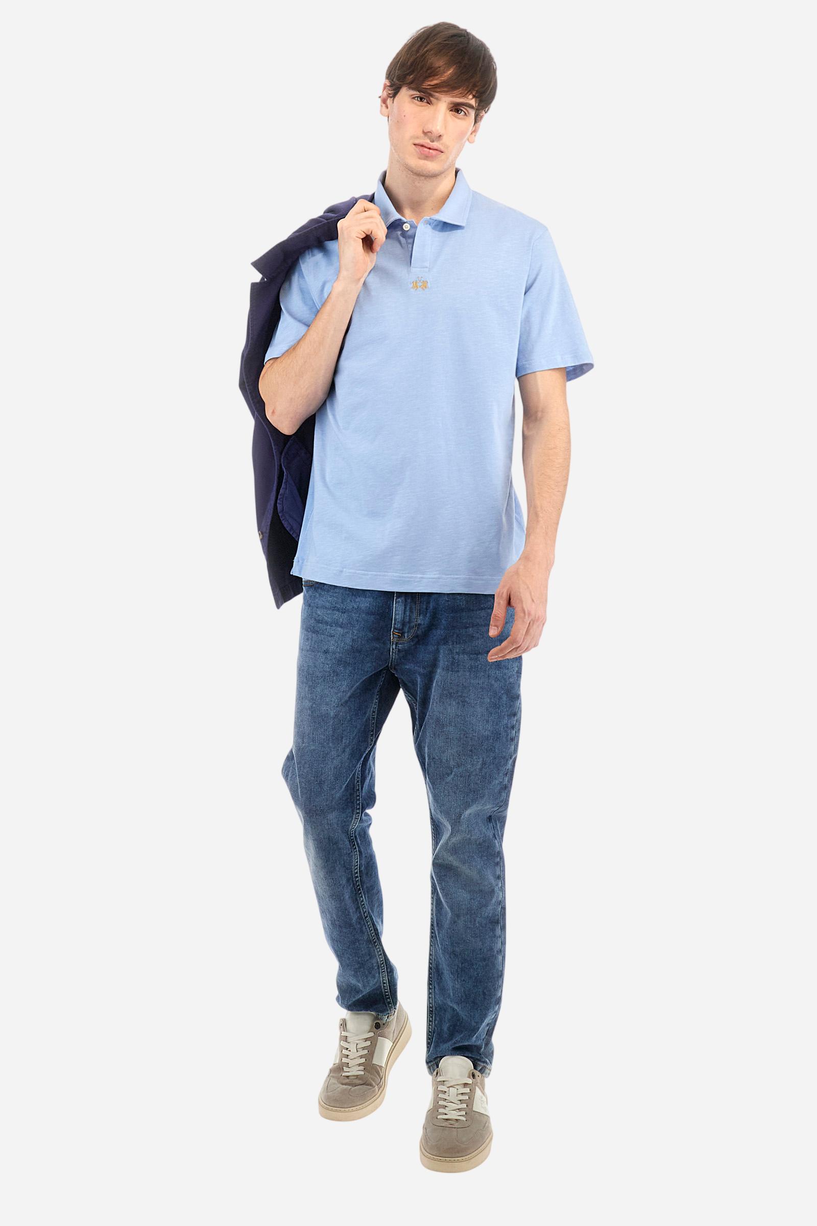 Men's short-sleeved polo shirt in a single colour, made of 100% cotton slub jersey. Fastens with a button. A fabric patch representing the garment's certificate is sewn onto the back. The logo is embroidered in contrast under the opening on the front. Comfort fit. The model is wearing a size L. - Vista Blue