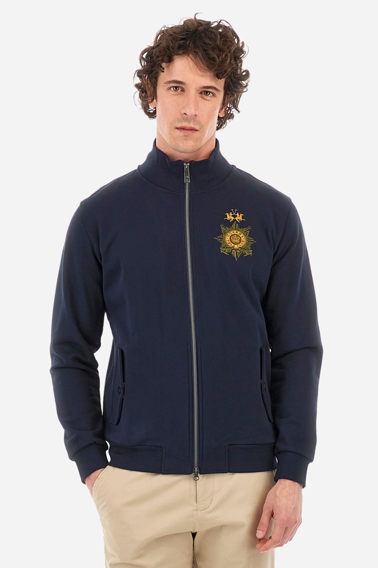 Men’s solid color long sleeve sweatshirt with full zip closure. Made of 100% cotton. High neck with drawstring, ribbed hem and cuffs. Double front pocket with button closure. Writing and large symbol on the chest identify the capsule collection. The fit is regular. The model wears a size L. - Navy