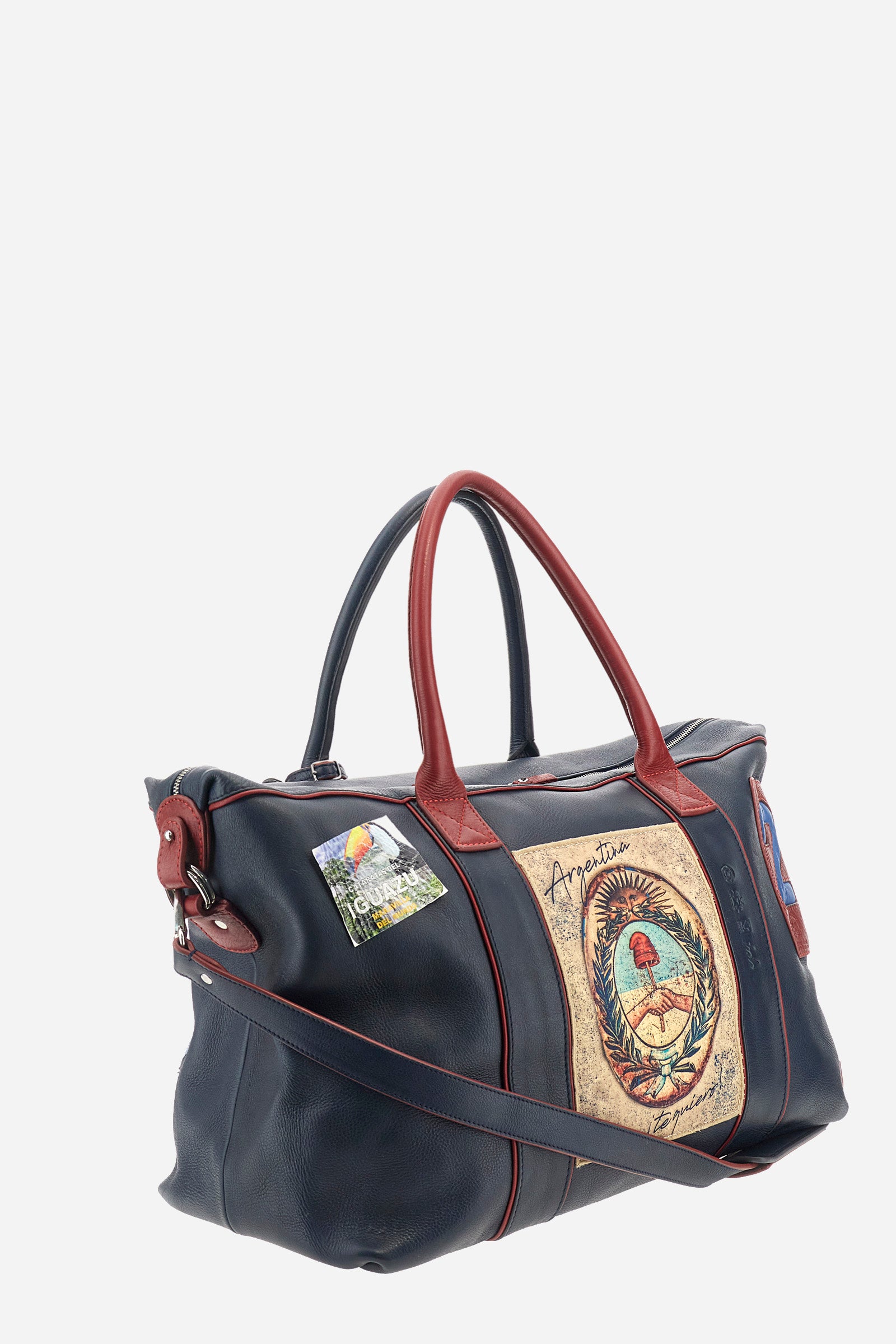 Unisex duffel bag in solid color, made of 100% leather. Iconic brand design, enriched with writings and patches. Finished with contrasting elements. Zip closure. Equipped with two handles and a removable shoulder strap. The front of the accessory features the La Martina writing and logo. The bag is adorned with stitched patches depicting landscapes and symbols related to Argentina. A leather address tag is attached to one of the handles. Dimensions (width x height x depth): 64x42x23 cm. - Navy