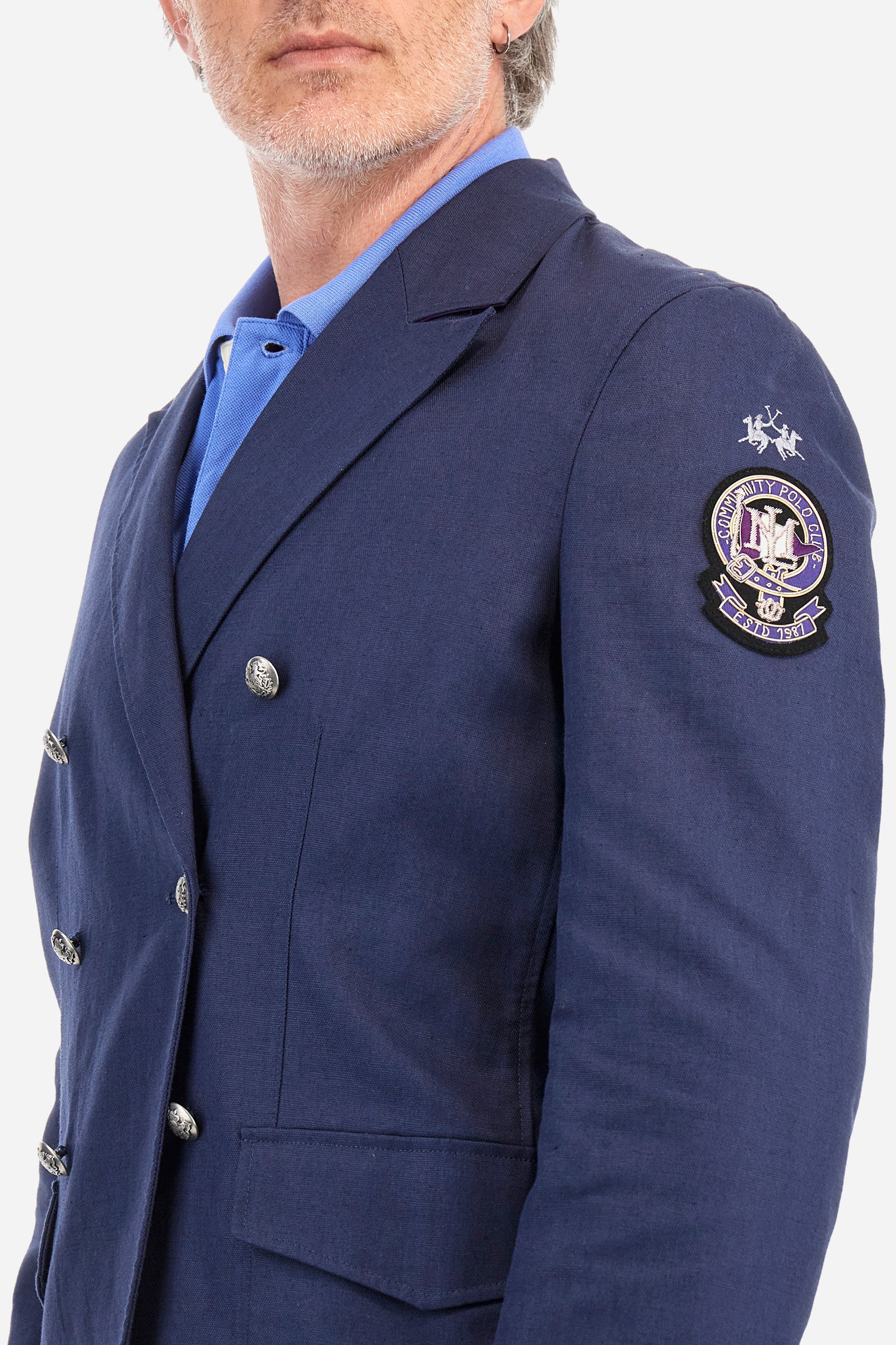 Men's long-sleeved double-breasted blazer in a single colour. Made of Oxford fabric, 50% cotton and 50% linen. Wide lapel neckline. The front patch pockets have rounded corners and feature a shaped flap. A subtle matching cotton trim is applied on the cuffs. Large patch in metallic thread applied on the left sleeve. The logo is embroidered tone-on-tone on the same sleeve. Regular fit. The model is wearing an Italian size 50. - Navy