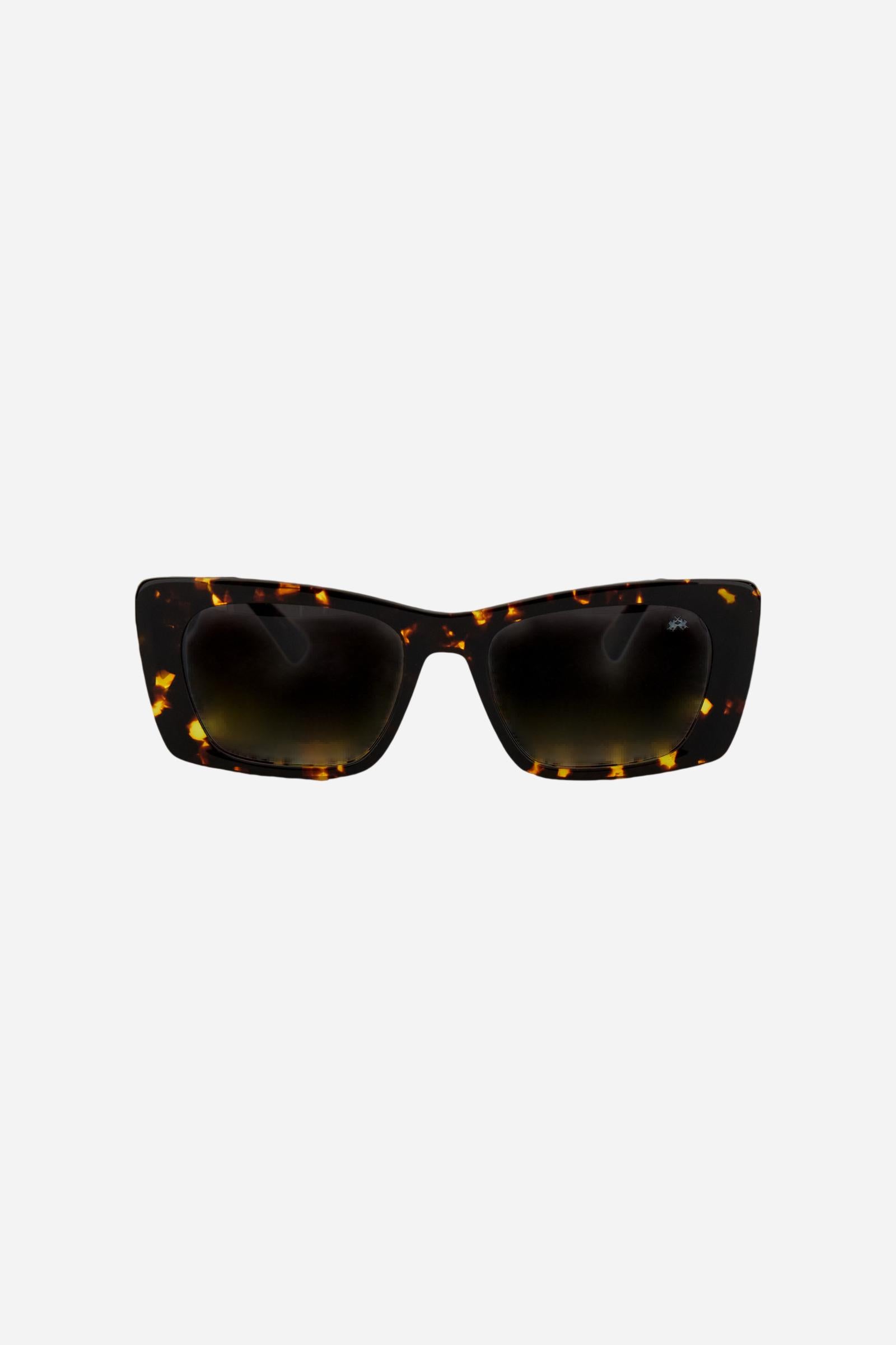 Women’s sunglasses crafted from acetate, available in a range of finishes that enhance the depth of color and the material’s natural shine. The dark nylon lenses, shaded upward, provide high UV protection and optimal visual comfort. The oversized rectangular silhouette recalls the iconic charm of the 1960s, reinterpreted through clean lines and contemporary proportions. Wide temples are embellished with the brand’s gold logo, a distinctive detail that completes the design with elegance. - CocoaBrown/AmberGo