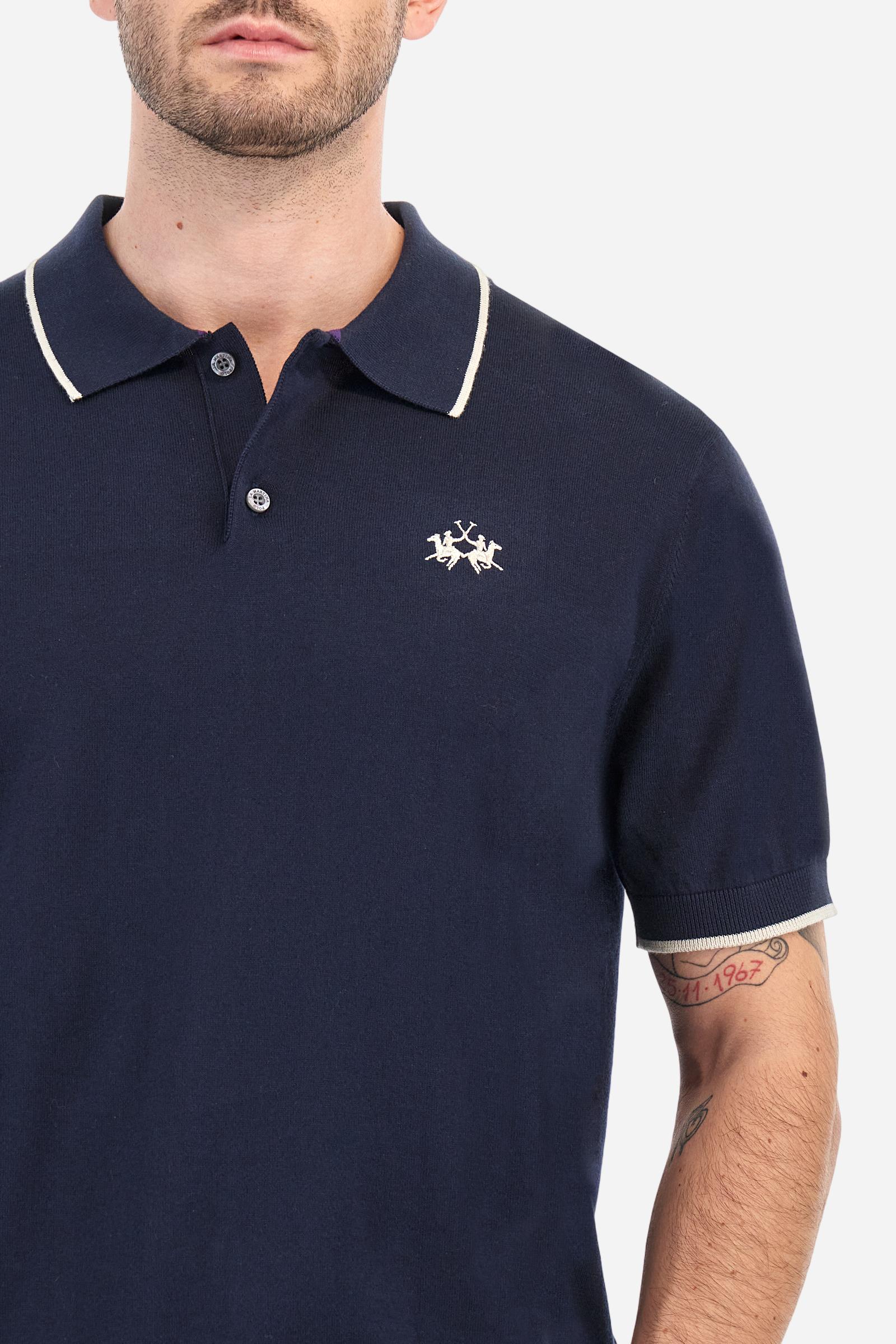 Single-colour men's polo shirt with short sleeves. Made of knitted cotton yarn. Two-button fastening and ribbed collar with contrasting stripes on the bottom. The cuffs of the sleeves are ribbed, as is the band at the bottom, which is embellished in the centre with a band featuring a herringbone stitch. A contrasting coloured jersey ribbon is applied to the inside of the collar. The logo is embroidered on the left side of the chest in contrasting thread. Regular fit. The model is wearing a size L. - Navy